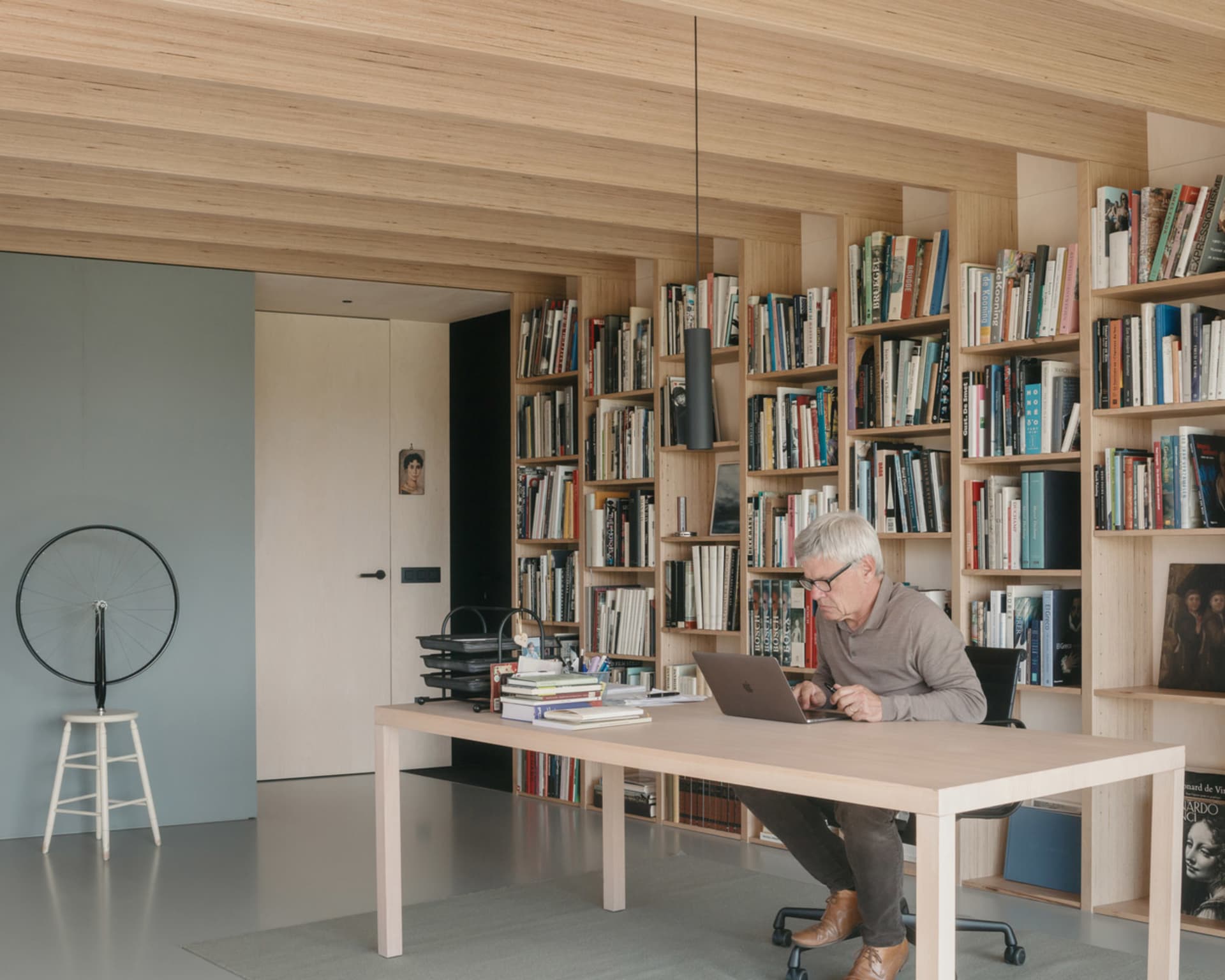 A modern home office featuring a wooden table and floating shelves filled with books.