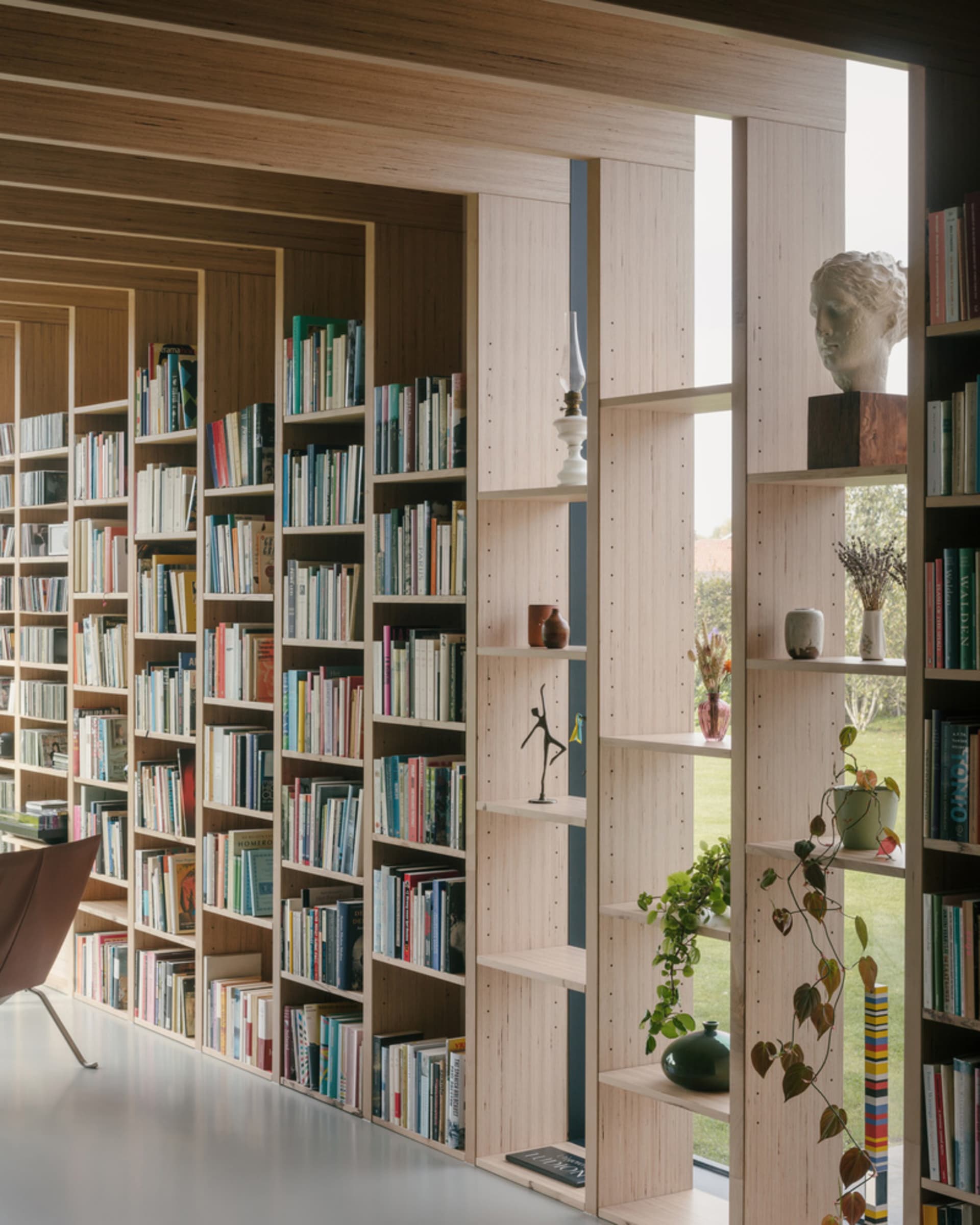 A modern library with tall bookshelves filled with books, sculptures, and plants.