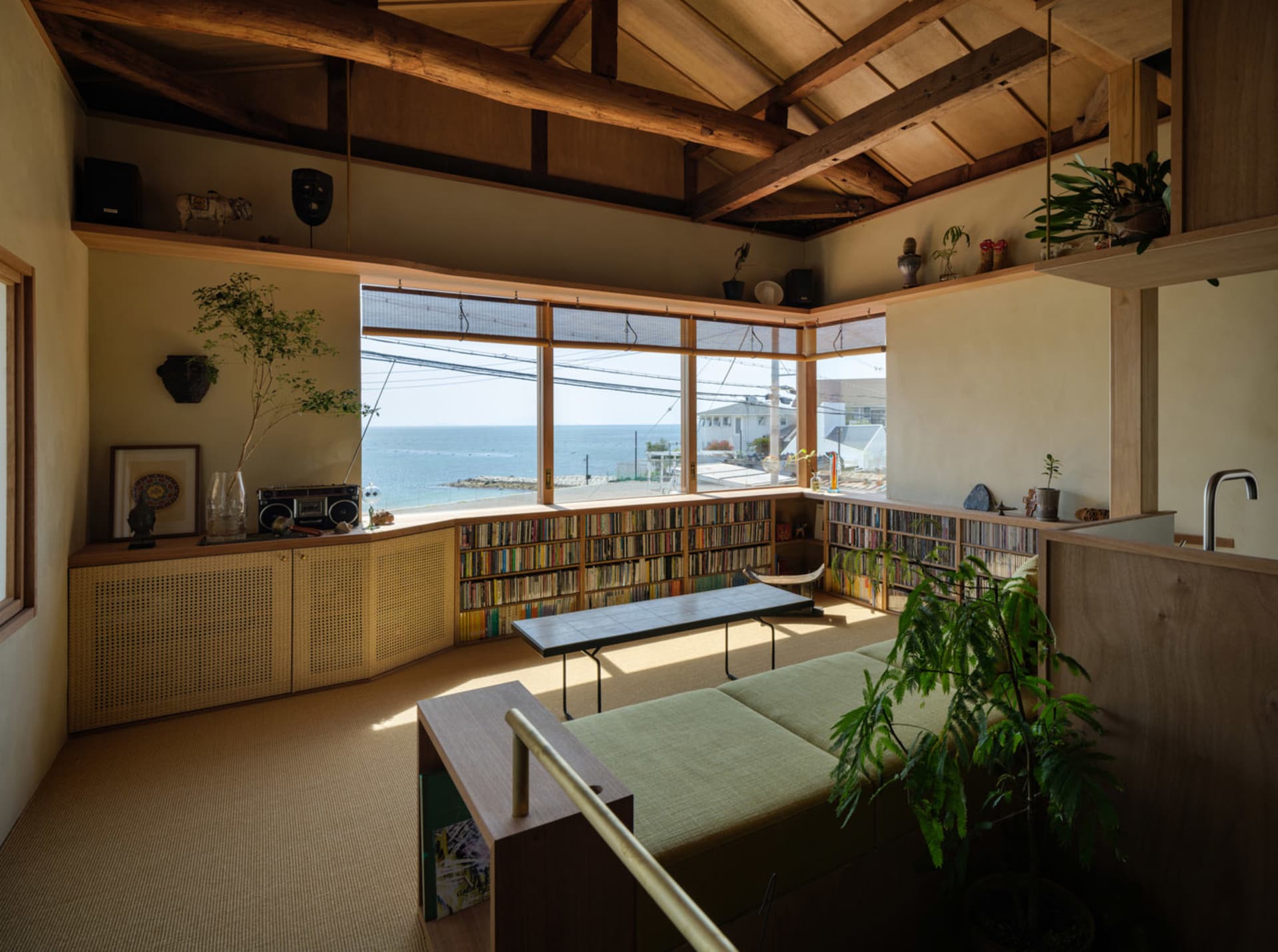 A modern living room featuring wooden furniture, glass panels, and a carpeted floor, with a view of the ocean through the lar