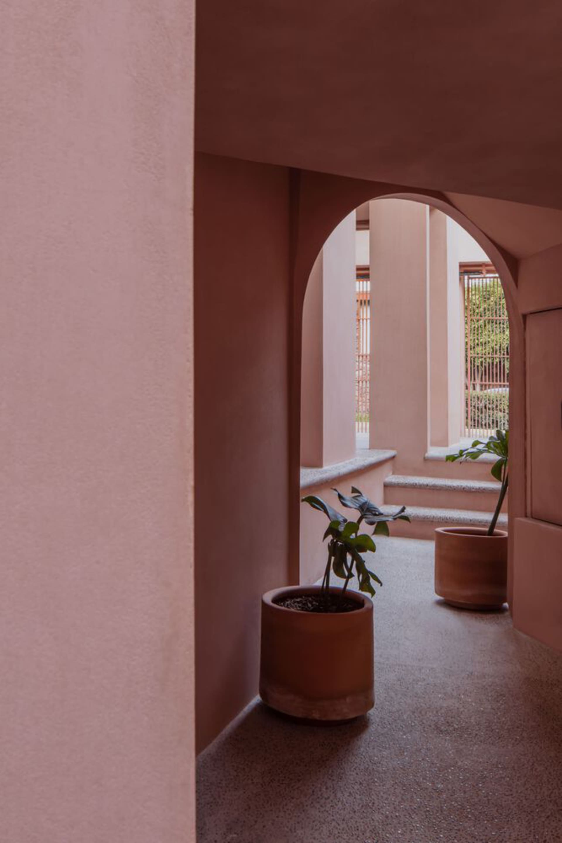 A modern architectural space featuring potted plants, arches, and terracotta flooring.