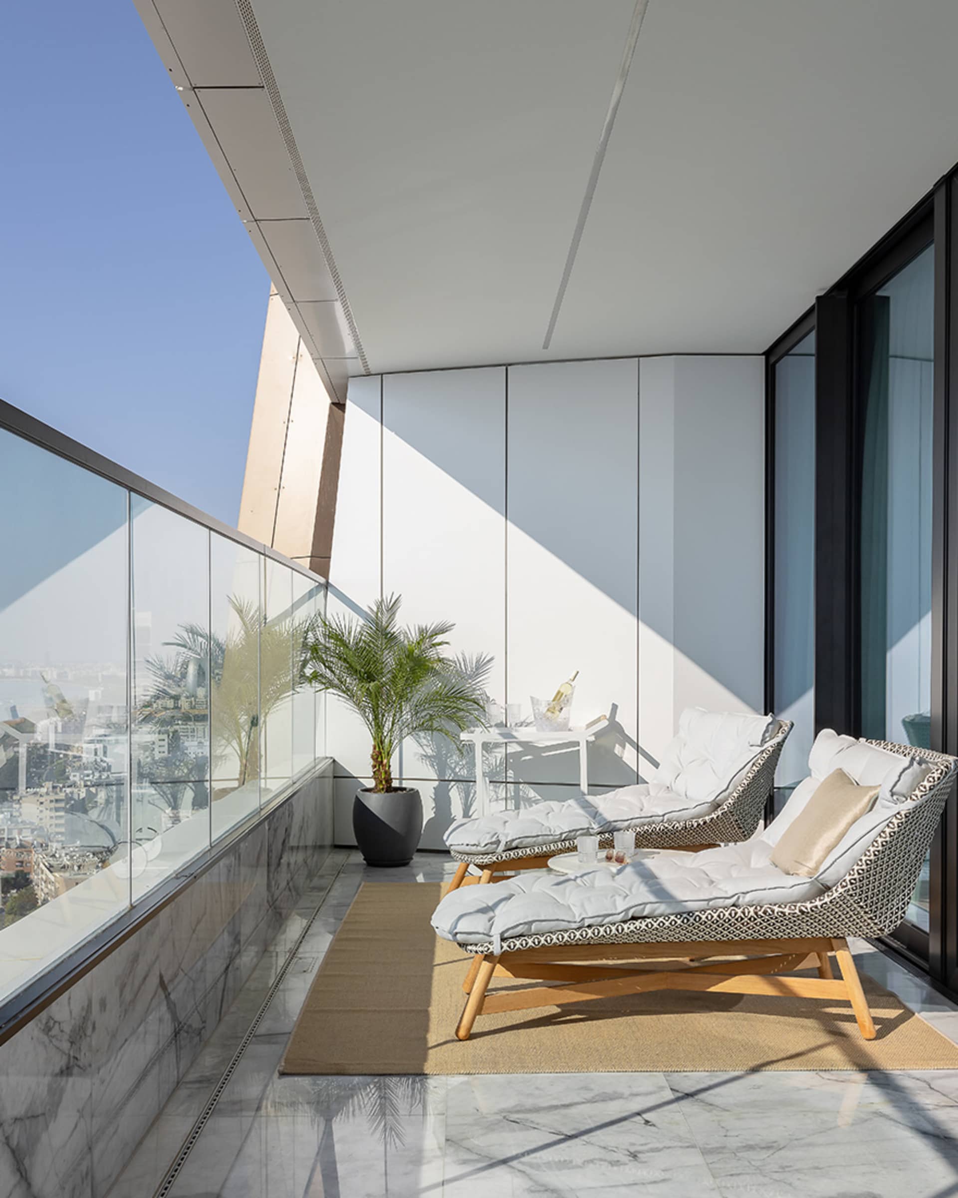 A modern balcony featuring marble and glass materials with comfortable seating arrangements.