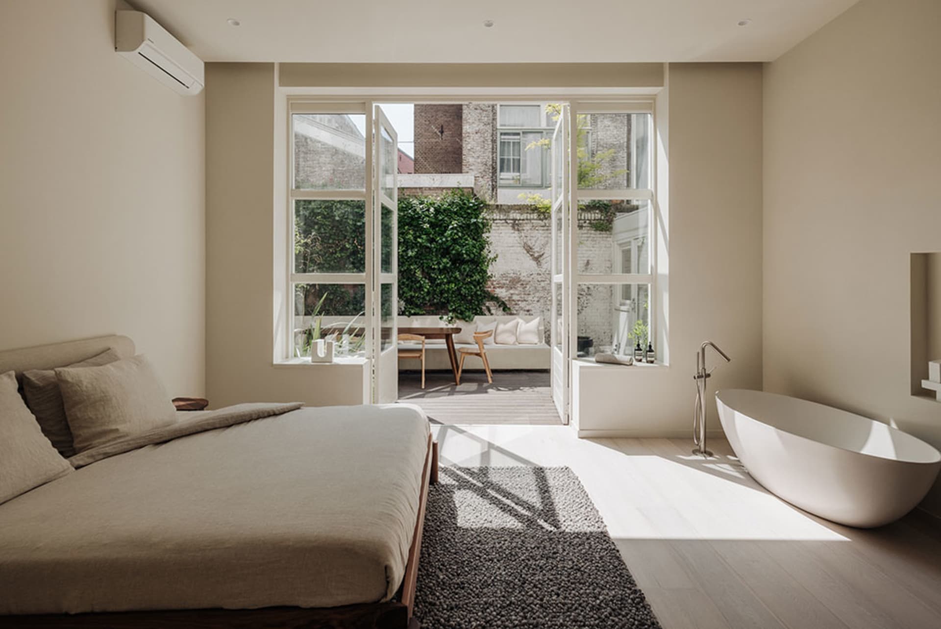 A modern bedroom with a large bed, free-standing bathtub, and large windows