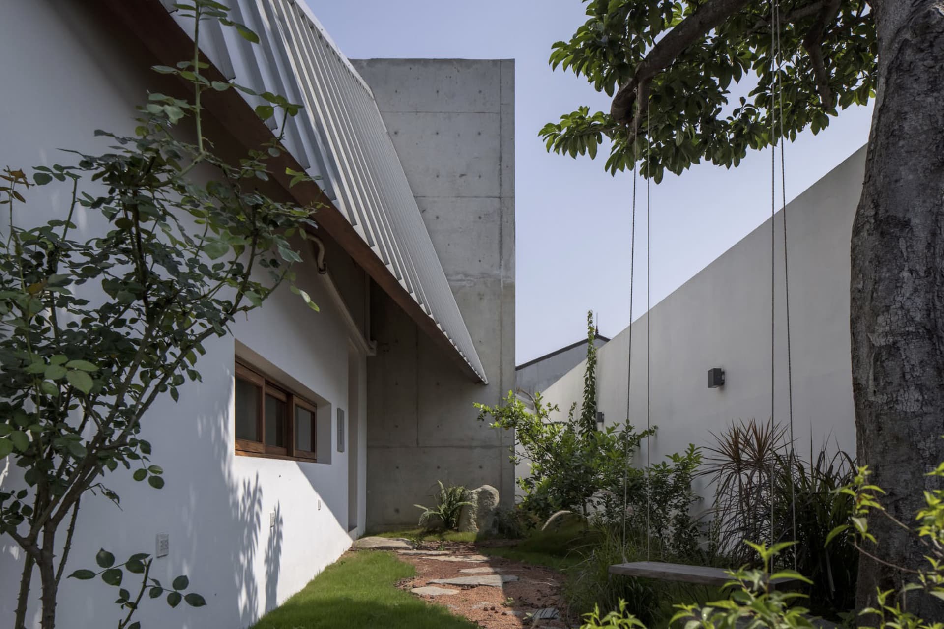 A modern private house with a concrete and glass exterior featuring a garden area and a tree.