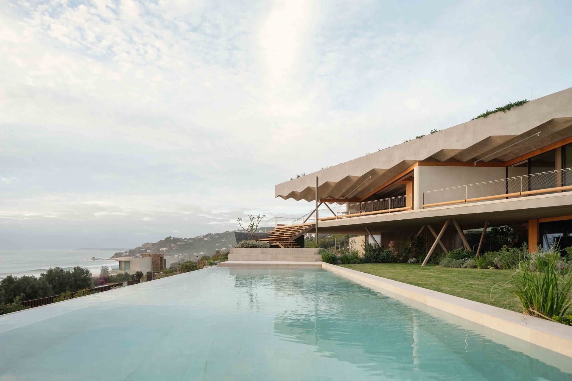 A modern residential house with a concrete exterior featuring a large outdoor infinity pool and ocean view.