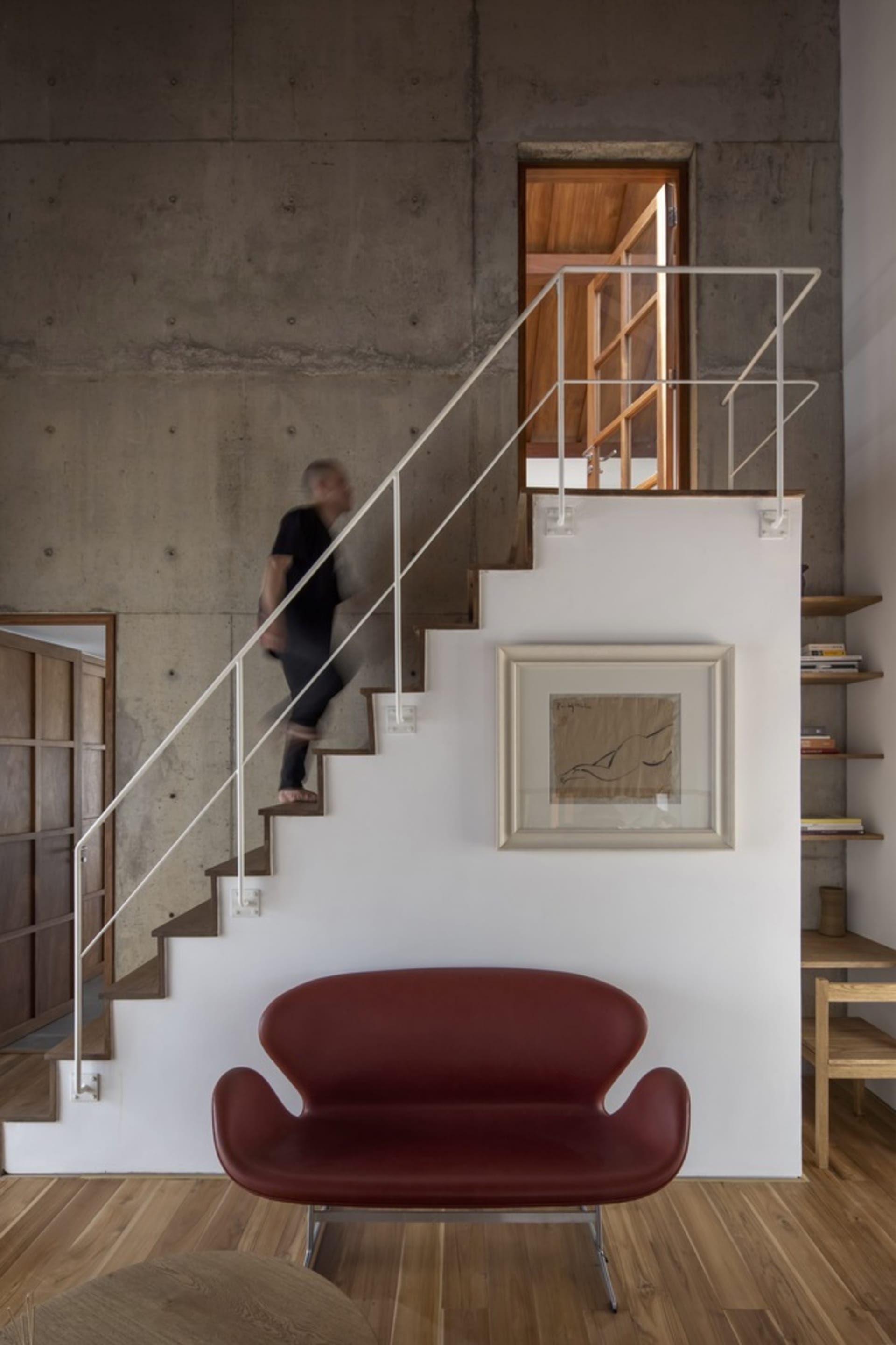 A contemporary living room with concrete walls, stairs, and a red sofa.