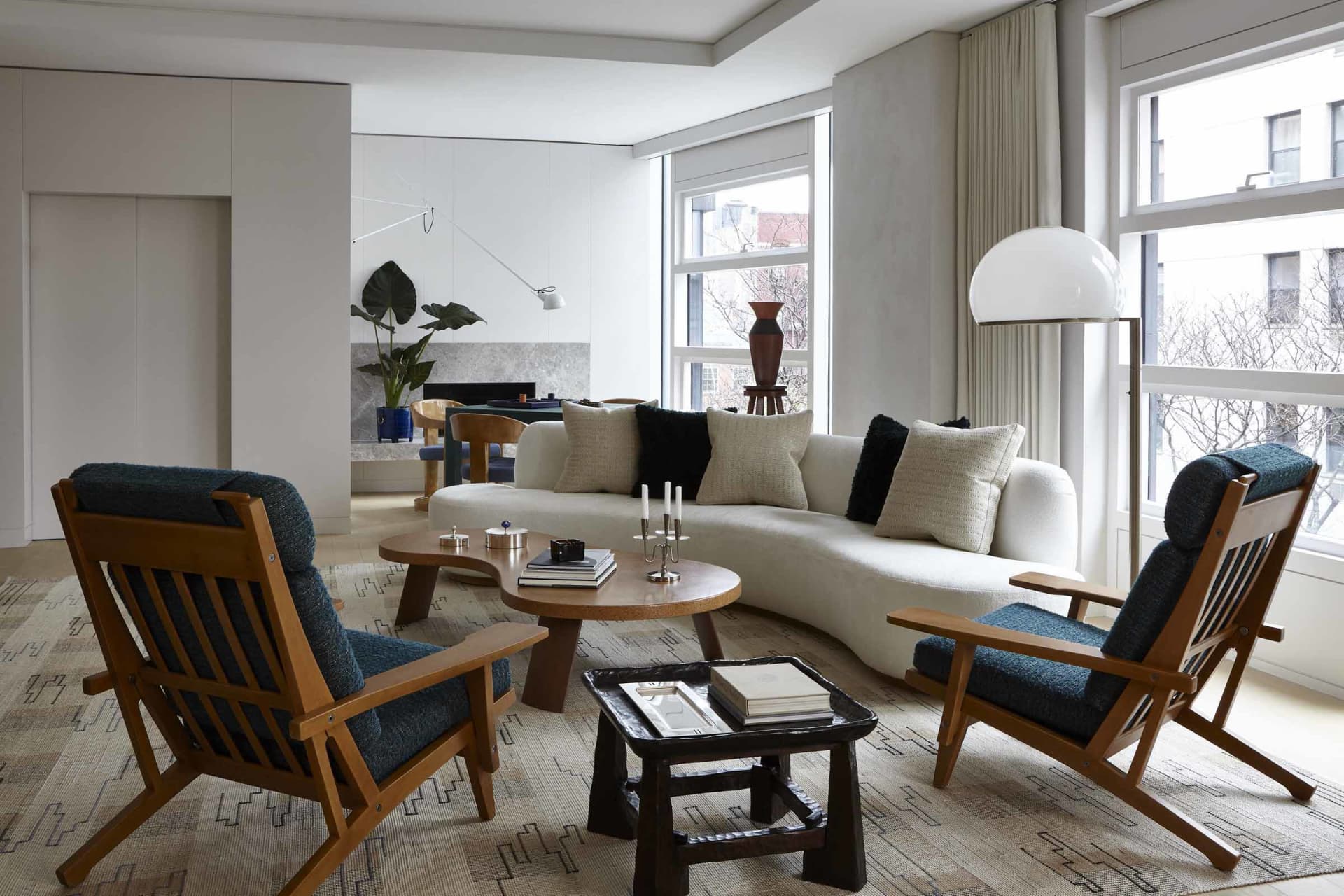 A modern living room featuring a curved white sofa, blue upholstered chairs, and a wooden coffee table with books and candles