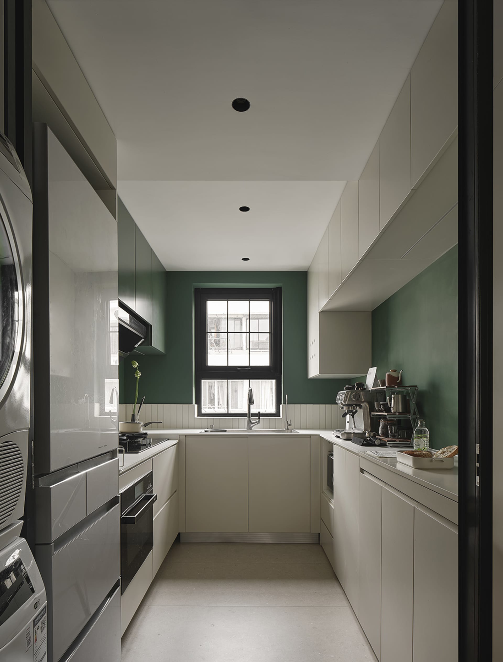 A modern minimalist kitchen with white cabinets, a large window, and green accents.
