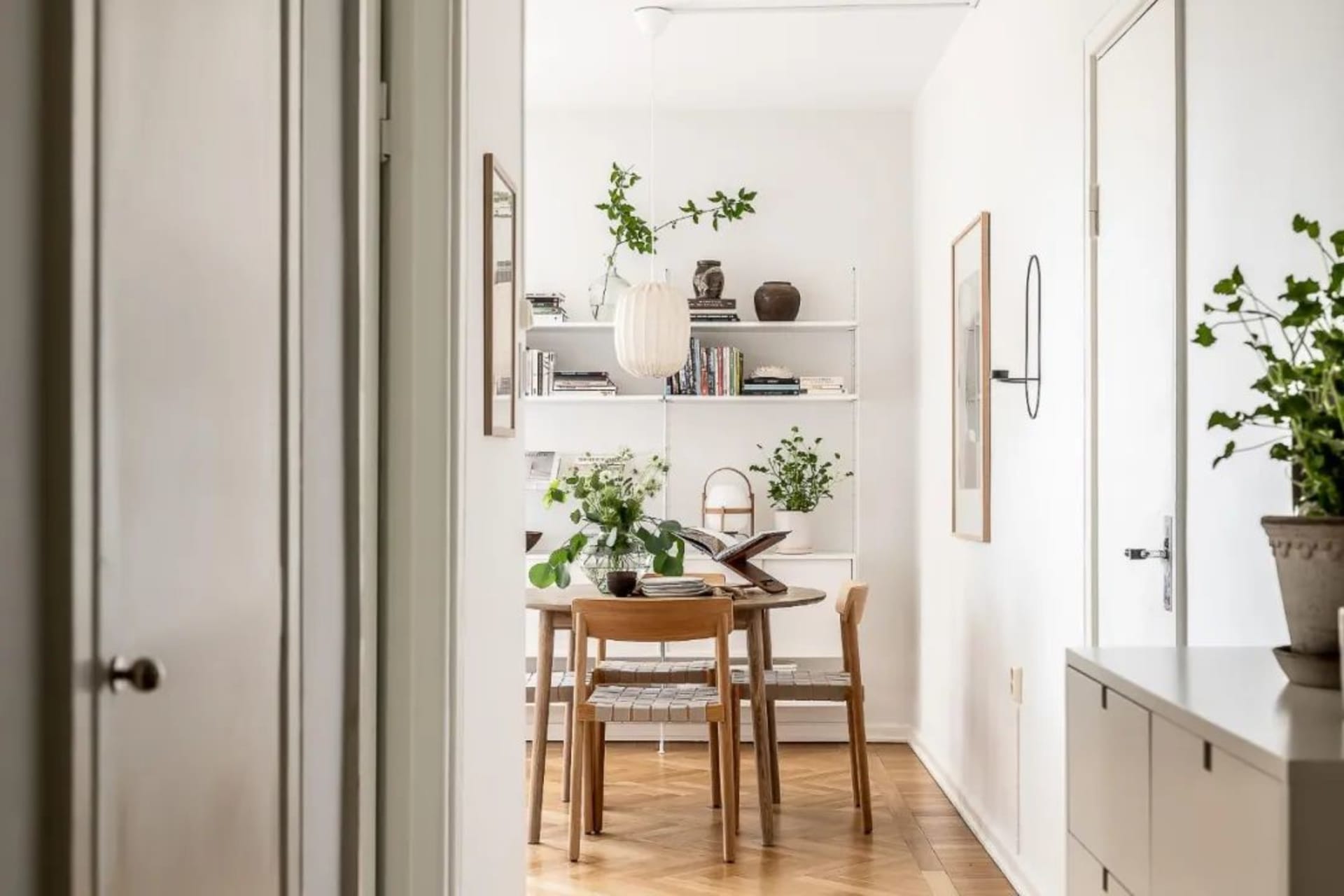 A minimalist dining room with a white interior, wooden floor, and a wooden table with chairs.