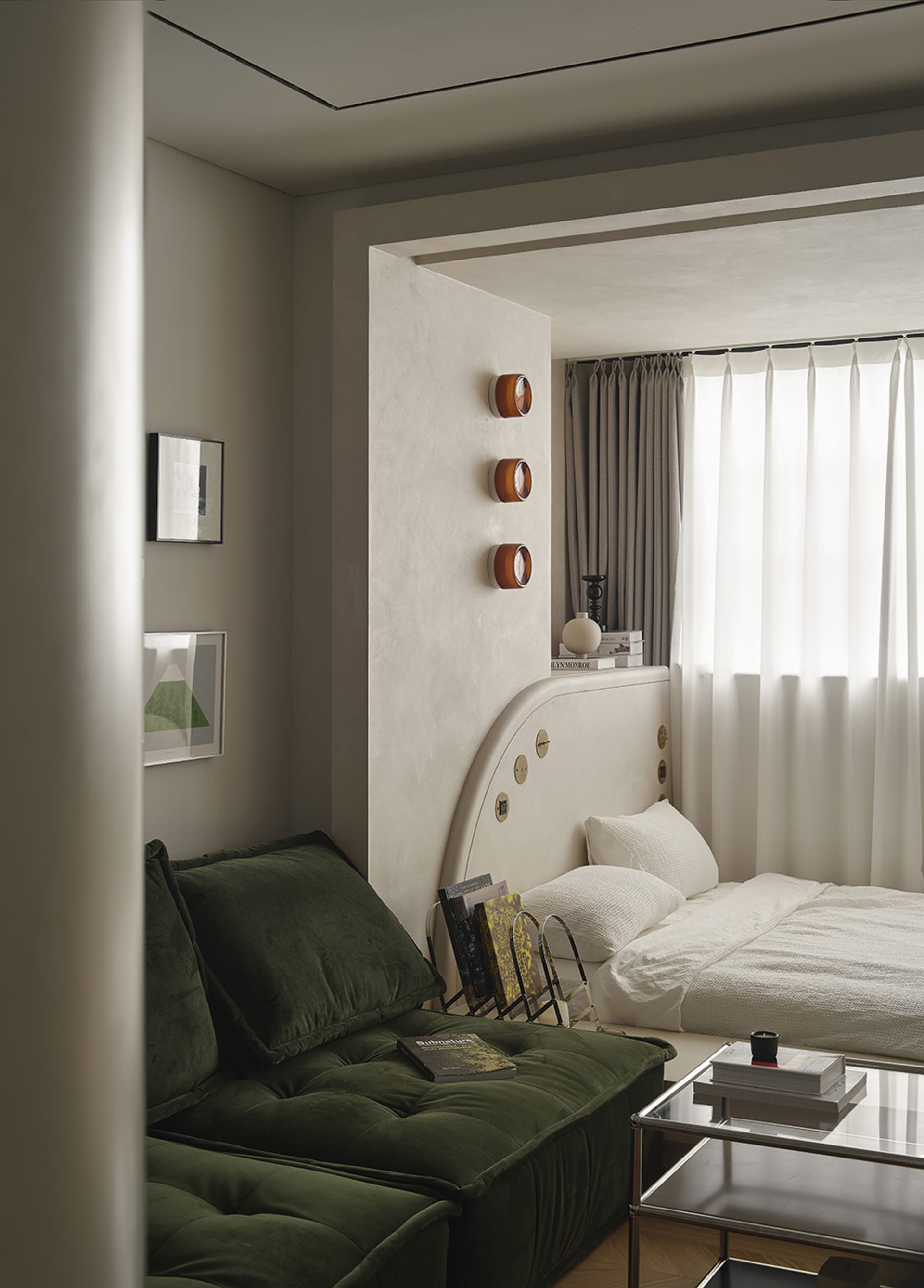 A modern bedroom featuring a bed with a fabric headboard and a glass coffee table with books and a candle.