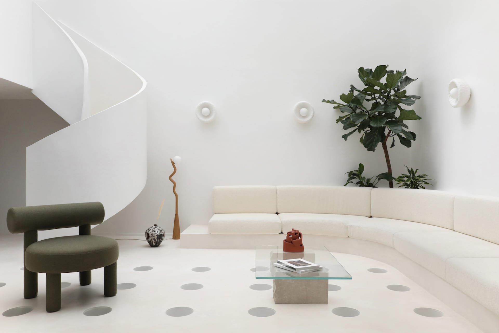 A modern minimalist living room featuring a white spiral staircase, a curved white sofa, a green armchair, and a glass coffee
