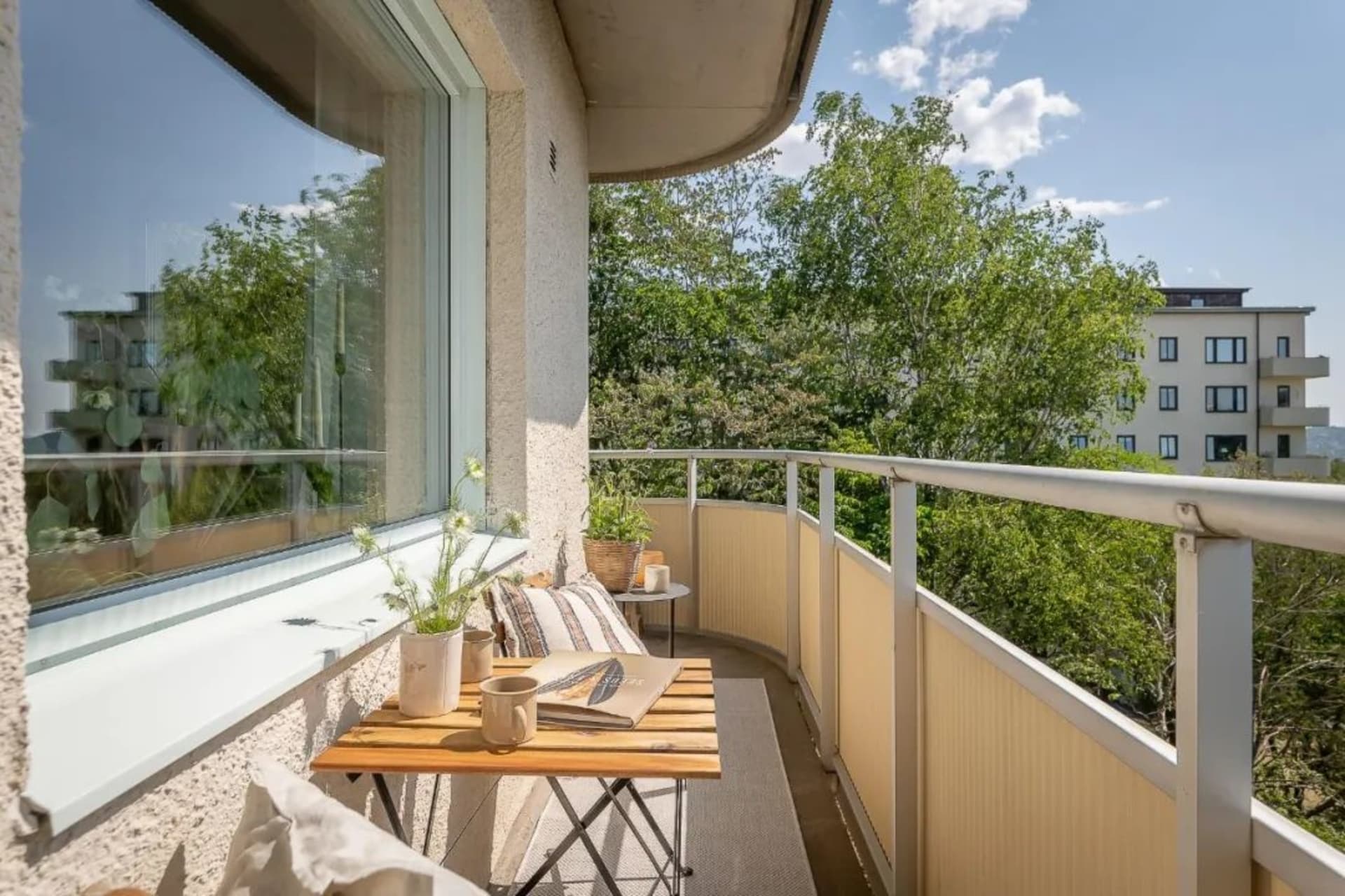 Outdoor balcony with wooden furniture, concrete floor, and greenery.