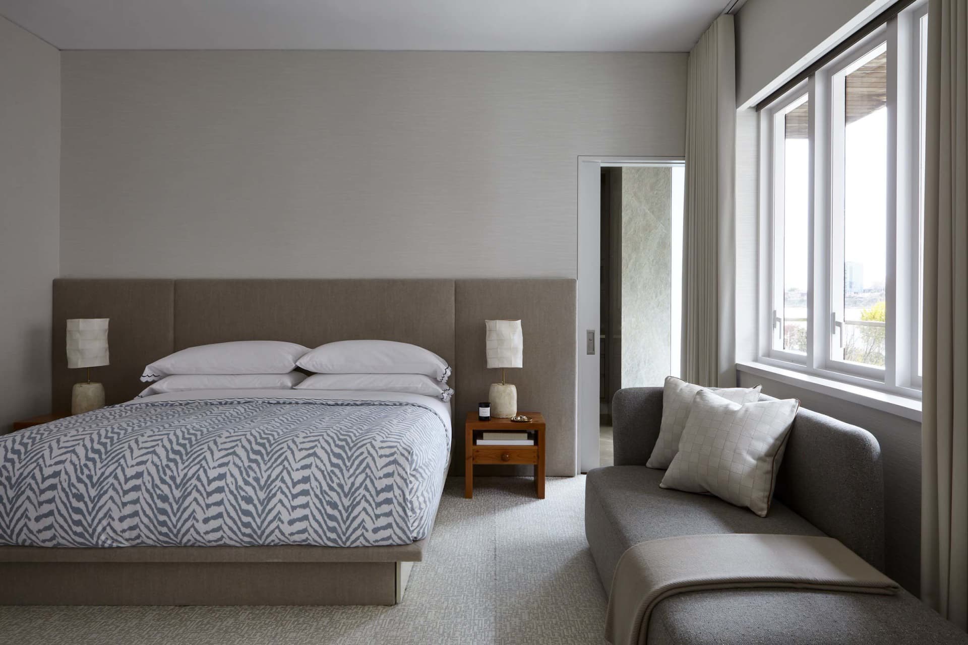 A contemporary bedroom furnished with a bed and a modern sofa, featuring a textured fabric headboard and sofa, and white and 