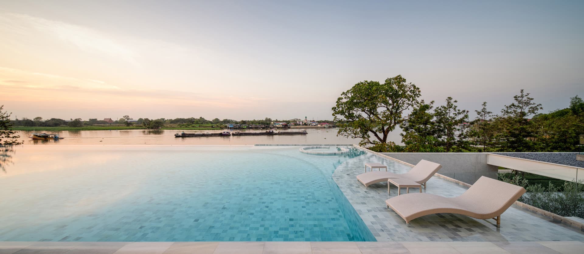 A luxurious residential poolside area with concrete features, surrounded by a serene view of a river.