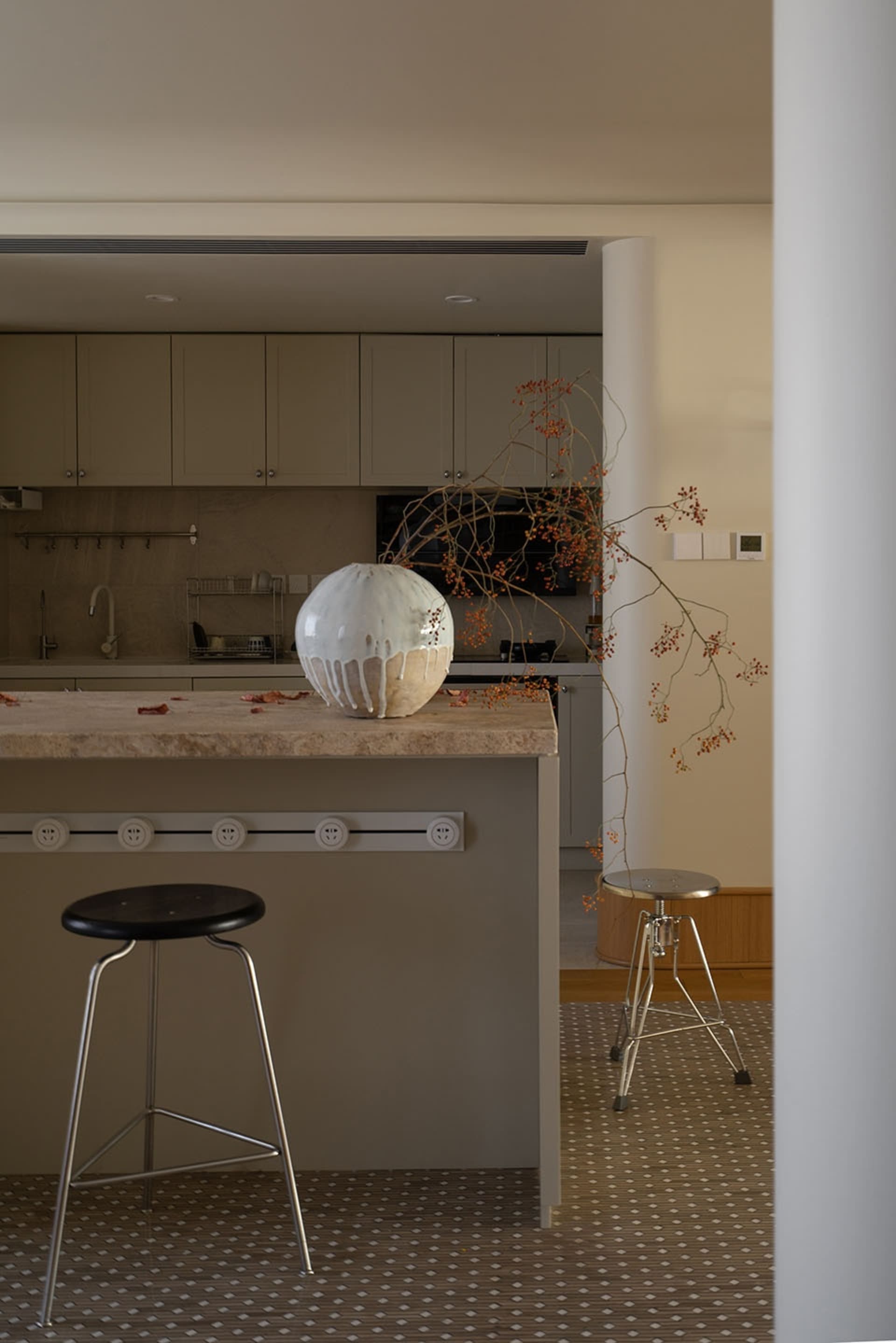 Minimalist kitchen with marble countertop and bar stools, featuring a large ceramic vase with intricate branch decorations.