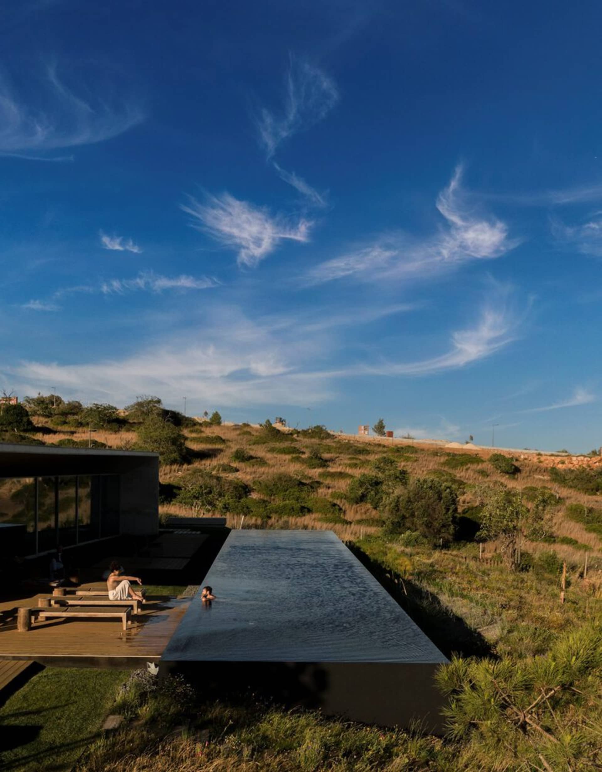 People lounging on a glass deck near a minimalist swimming pool.