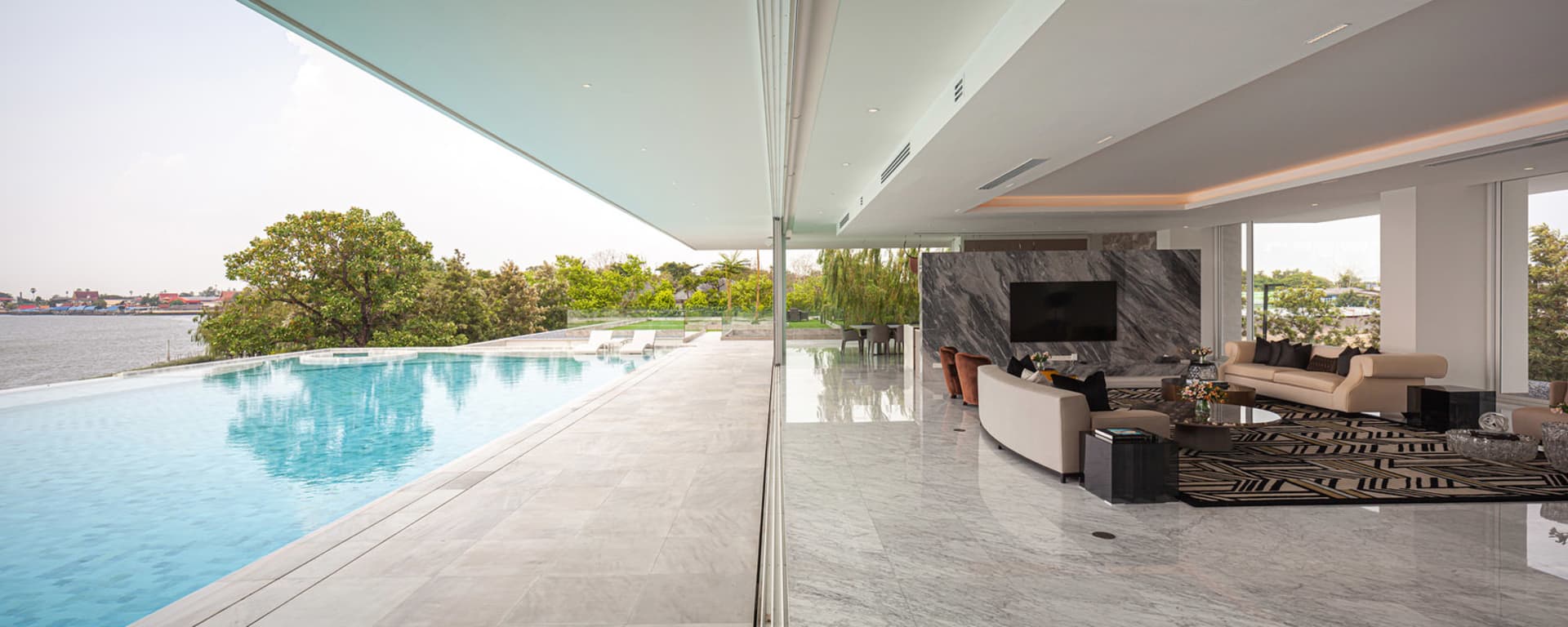 Modern living room featuring a sofa, coffee table, and television set with a view of a pool and greenery outside.