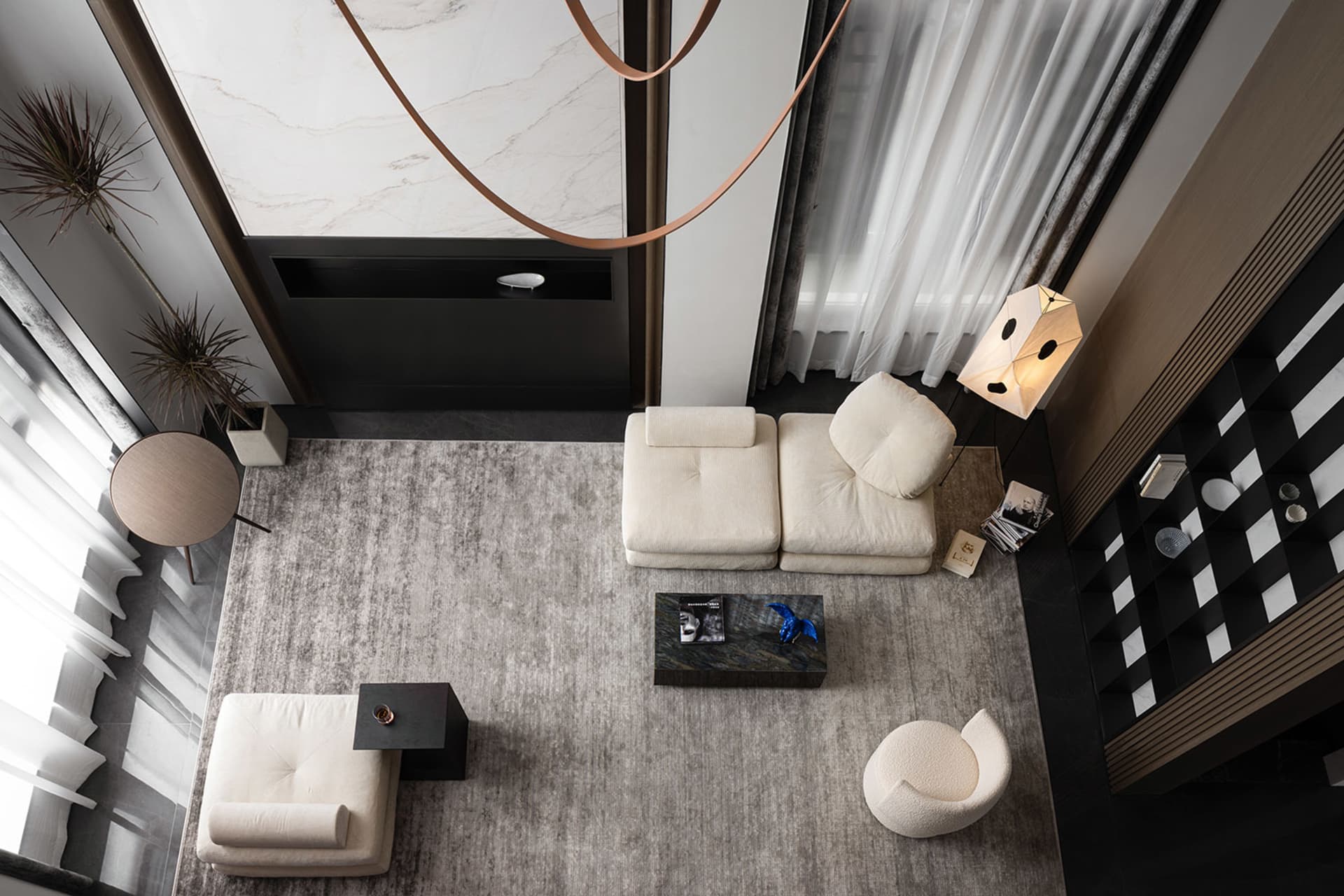 A modern living room featuring a white sofa, an armchair, a coffee table, and a bookshelf with magazines. The room has marble