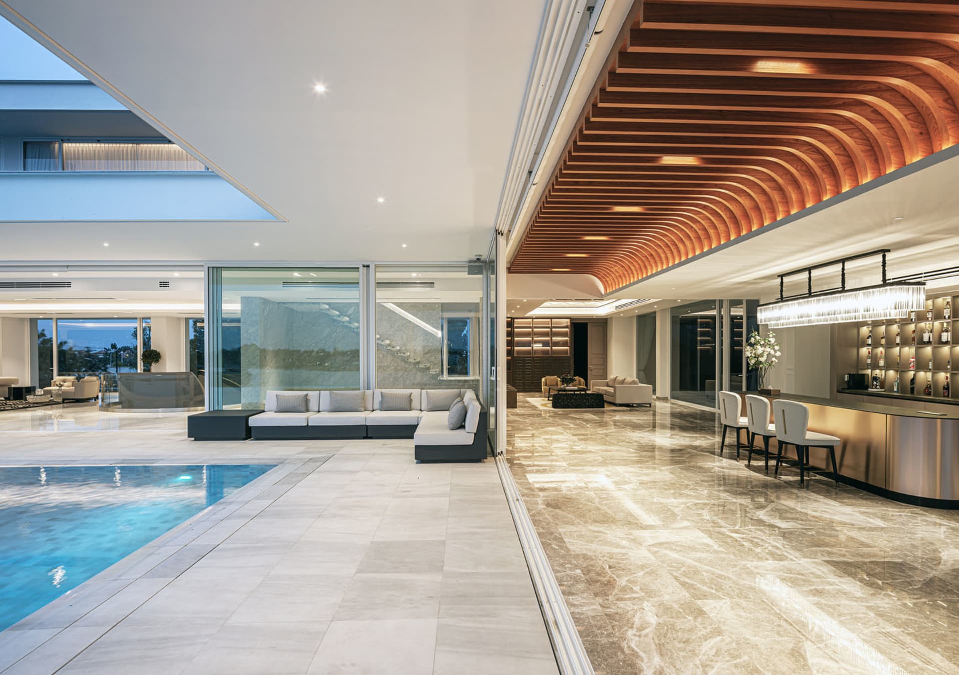 A modern, luxurious living room with a glass extension connecting to an outdoor pool area.