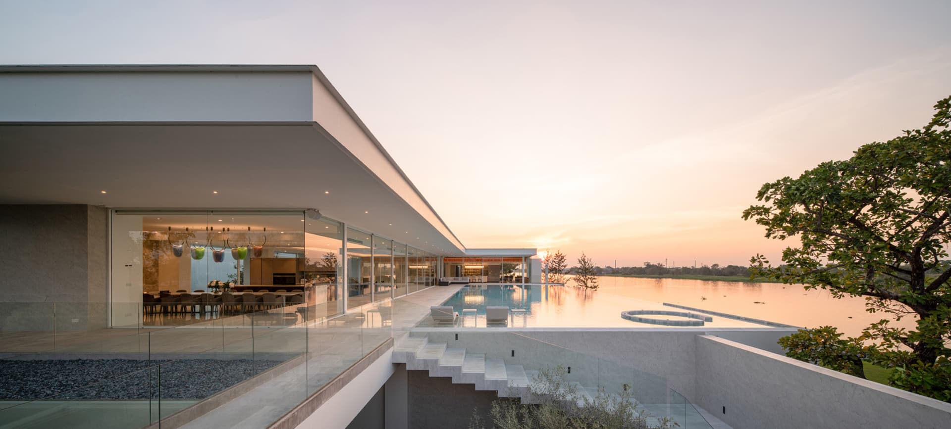 A modern residential building with glass walls and a rooftop pool overlooking a serene lake.