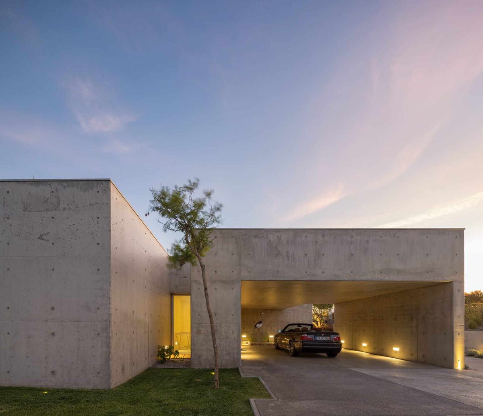 A modern, minimalist house with a concrete facade, featuring an indoor carport with a car parked inside.