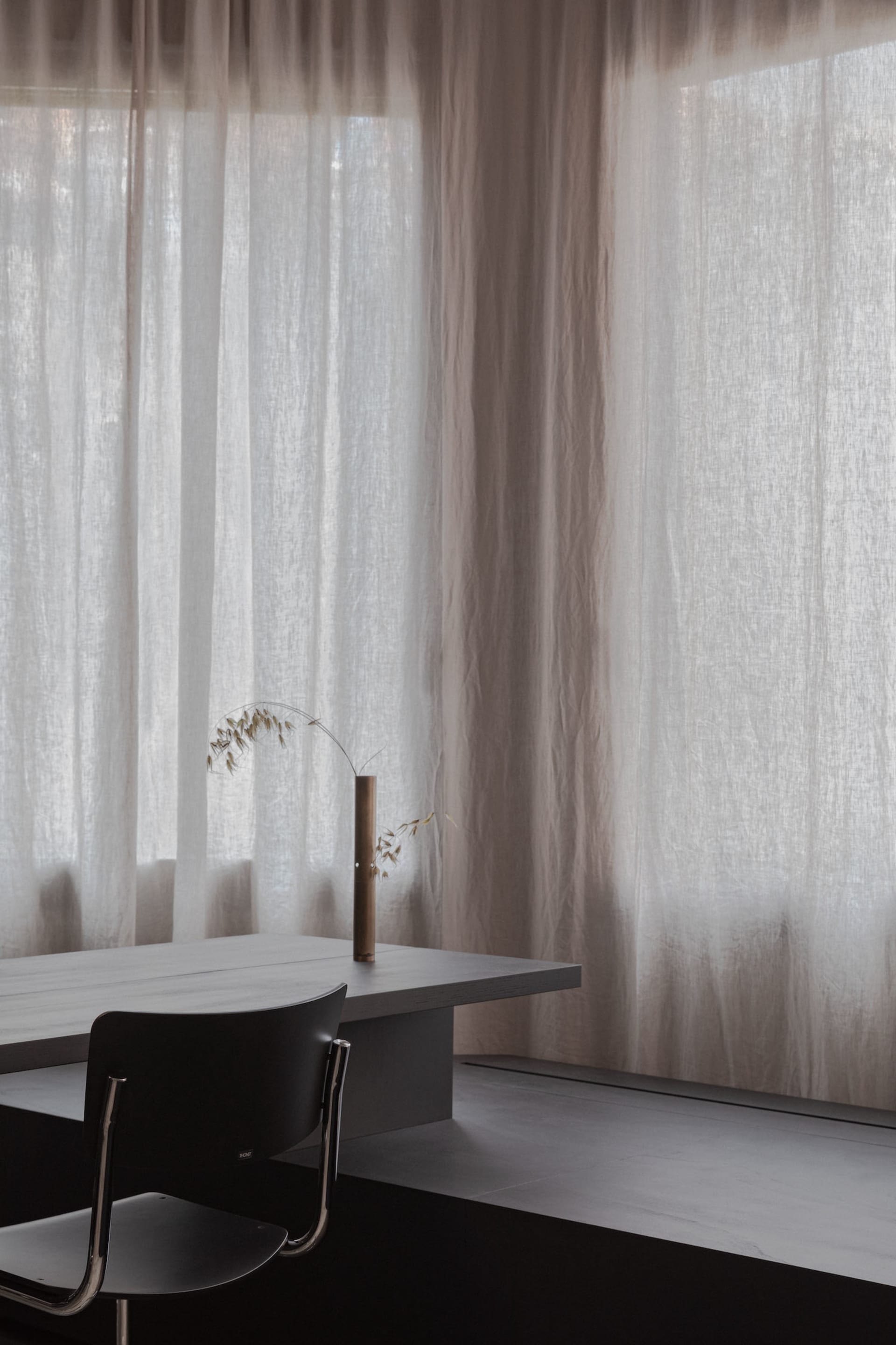 Minimalist room with transparent curtains, wooden table, and black chair