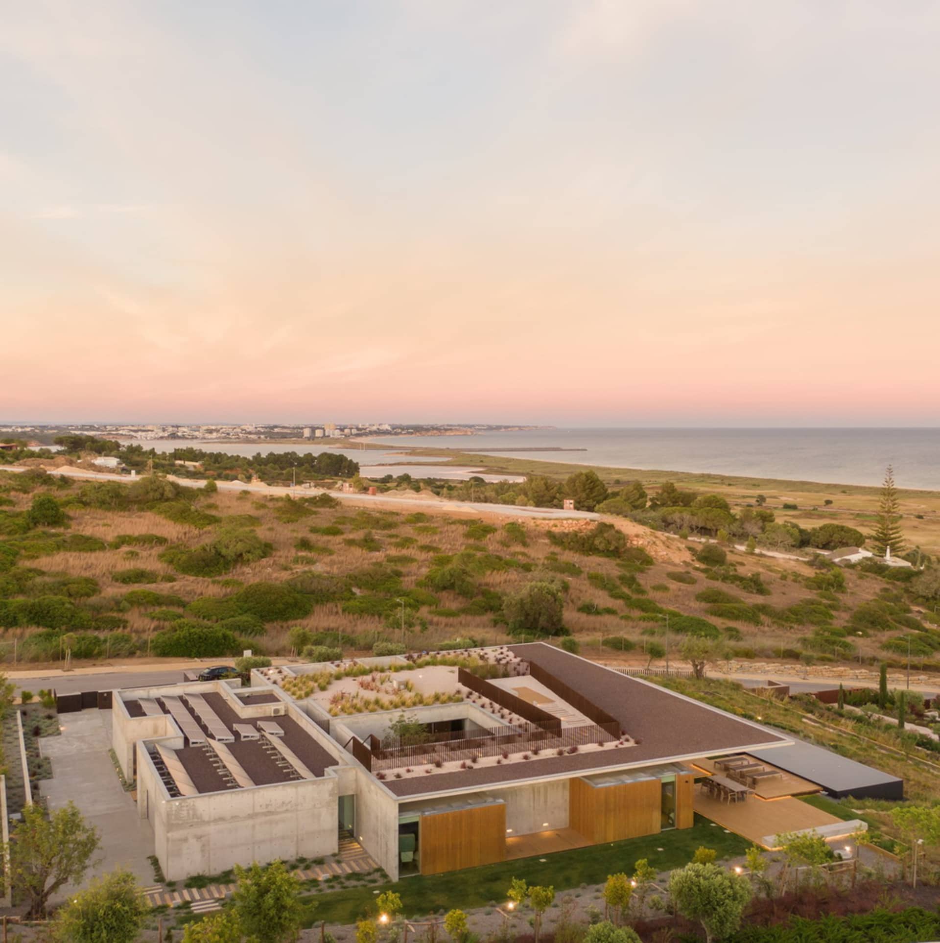 Modern house with concrete and wooden exterior against a scenic coastal backdrop at sunset.