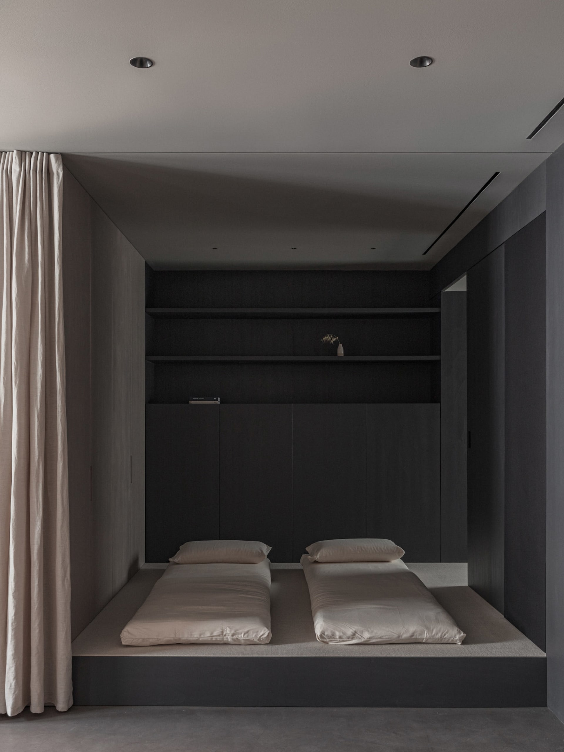 A minimalist bedroom with black wooden furniture and beige bedding.