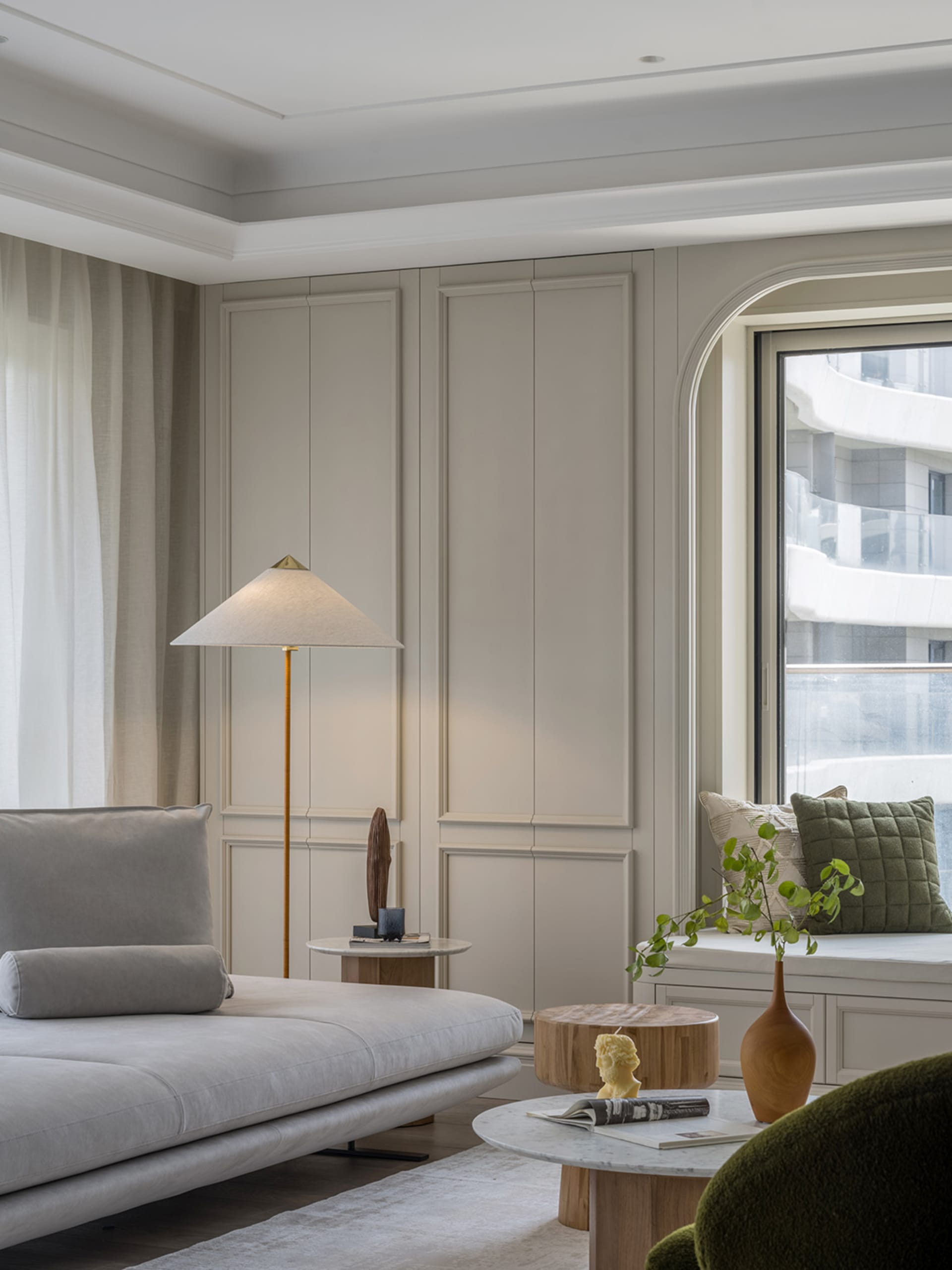 A modern interior with neutral tones featuring a minimalist sofa, a floor lamp, a coffee table, and green cushions.