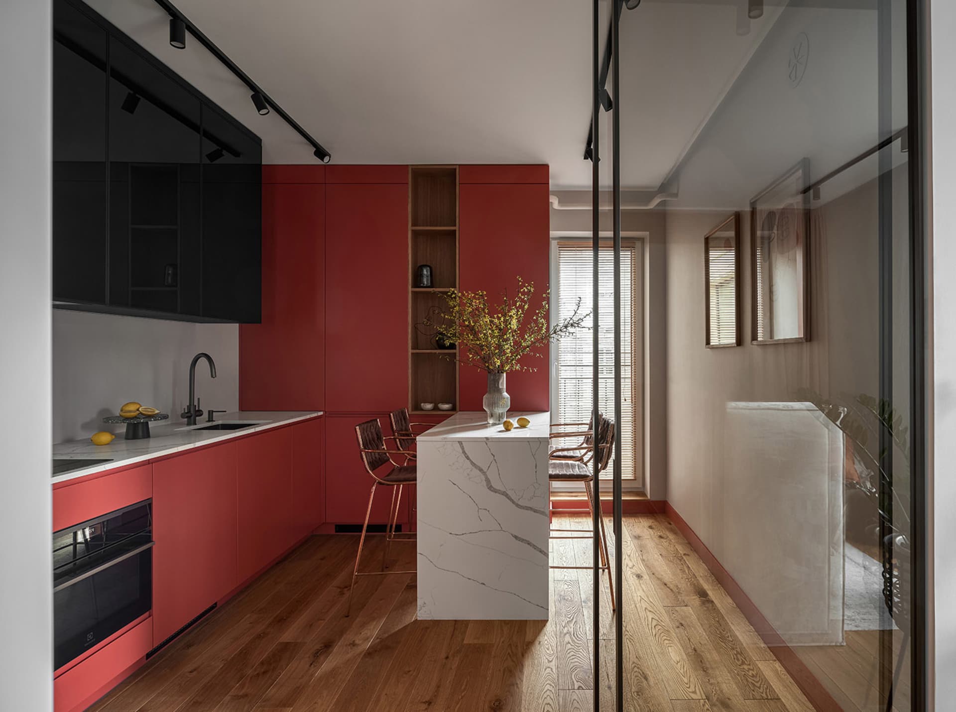 A modern kitchen featuring red cabinets, white marble top, and wooden flooring.