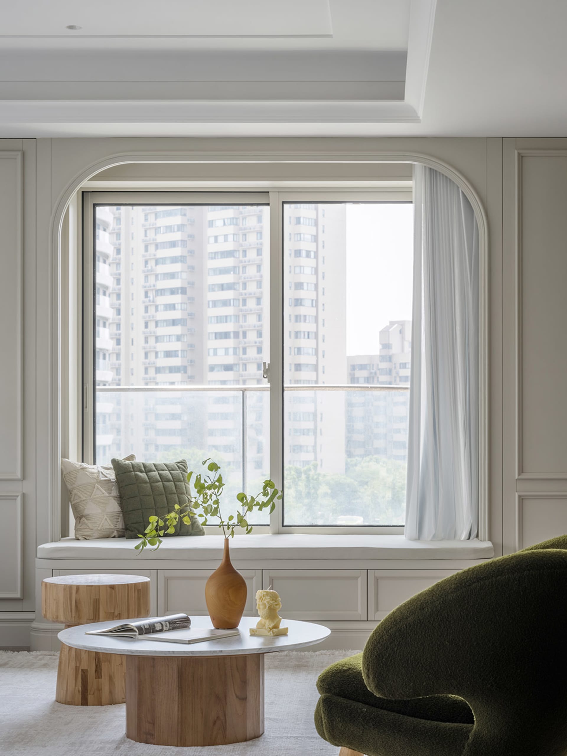 A minimalist living room with clean lines, a large window showcasing urban architecture, and neutral-toned furnishings.