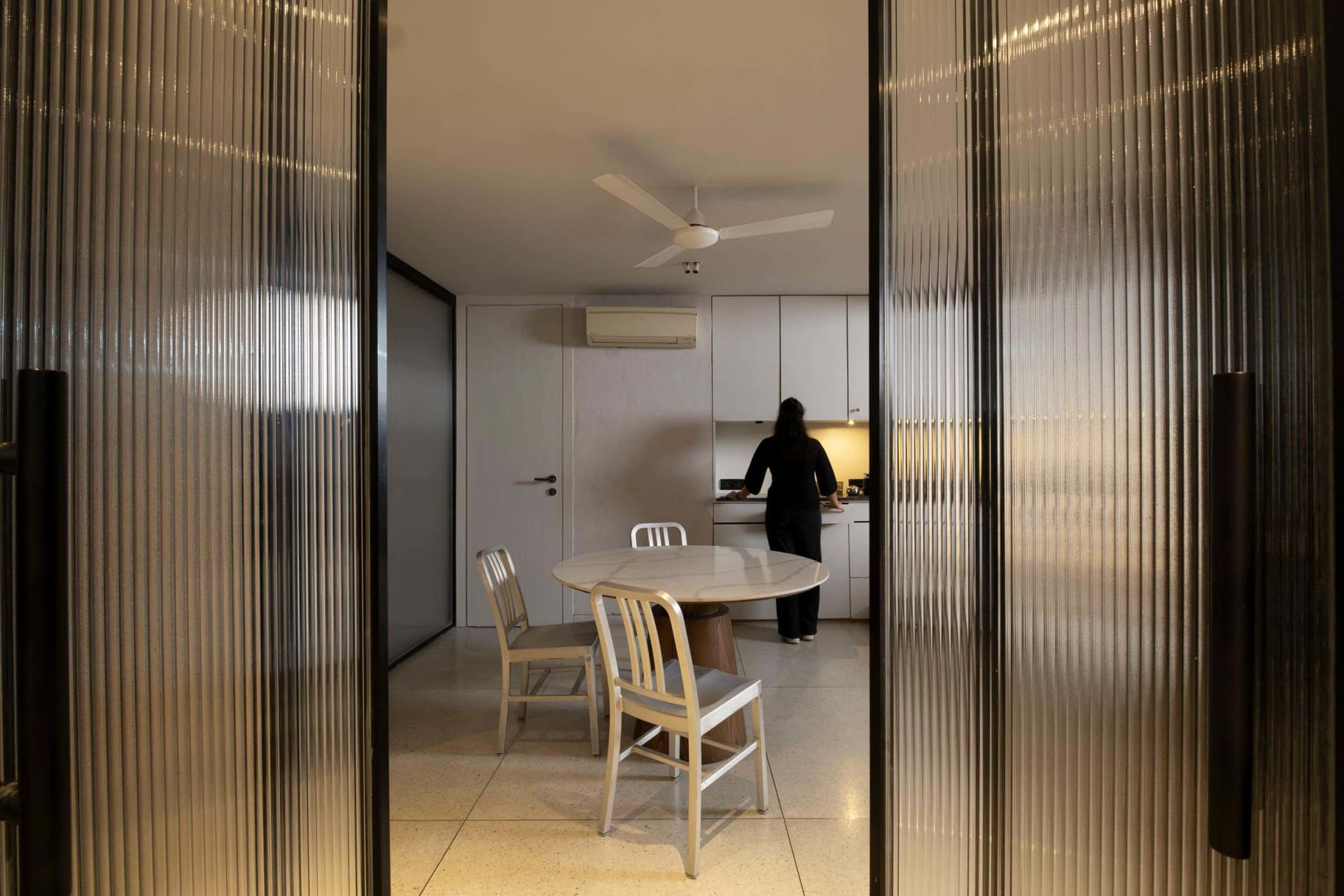 A minimalist kitchen featuring a glass and stone blend round dining table with white chairs.