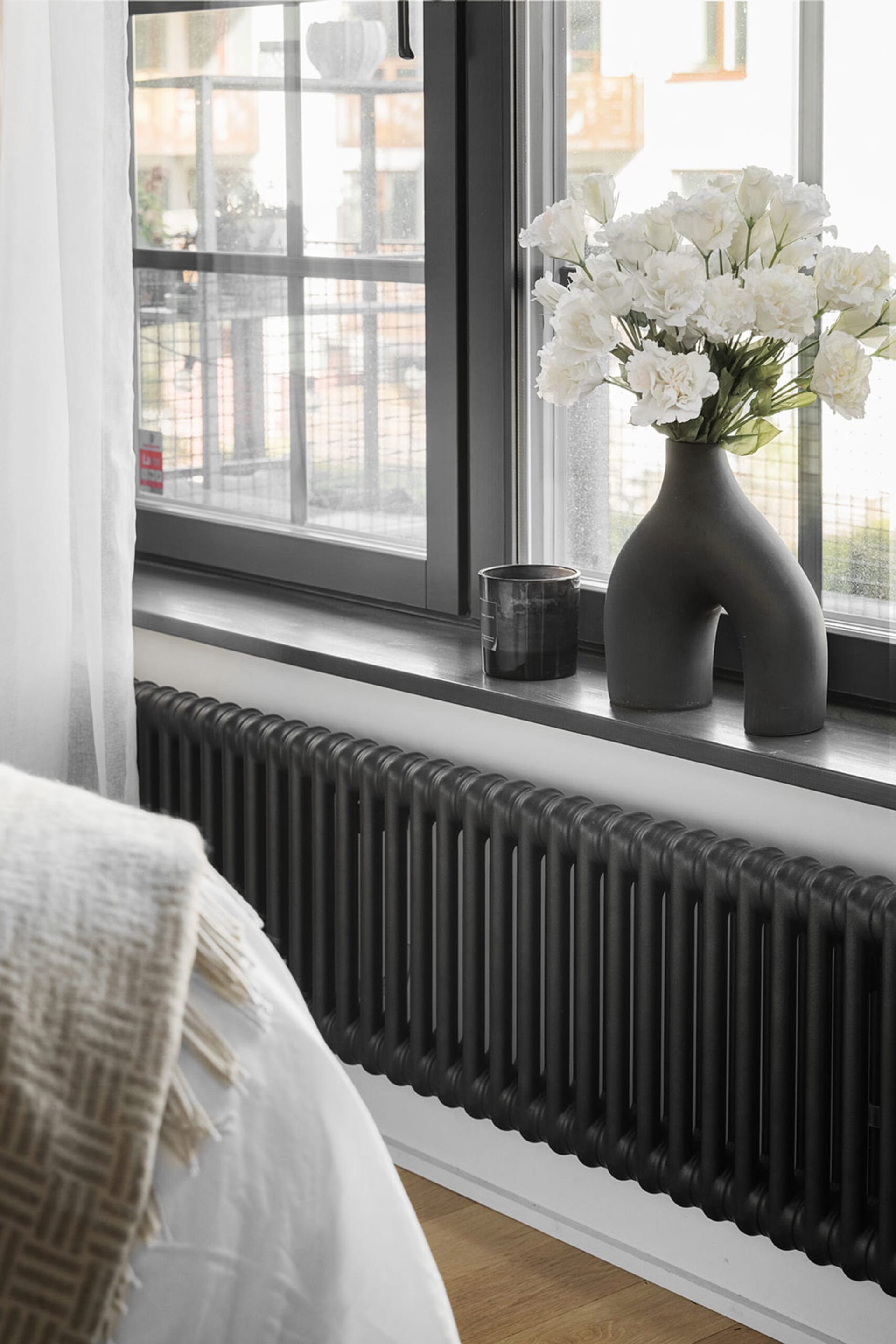 Modern bedroom featuring a black radiator, window, and flower vase.