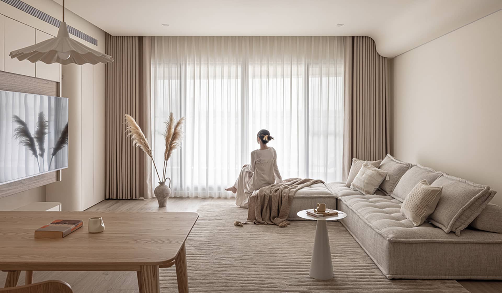 A minimalist living room with neutral-toned fabric furniture and textiles, featuring a L-shaped couch, a low coffee table, an
