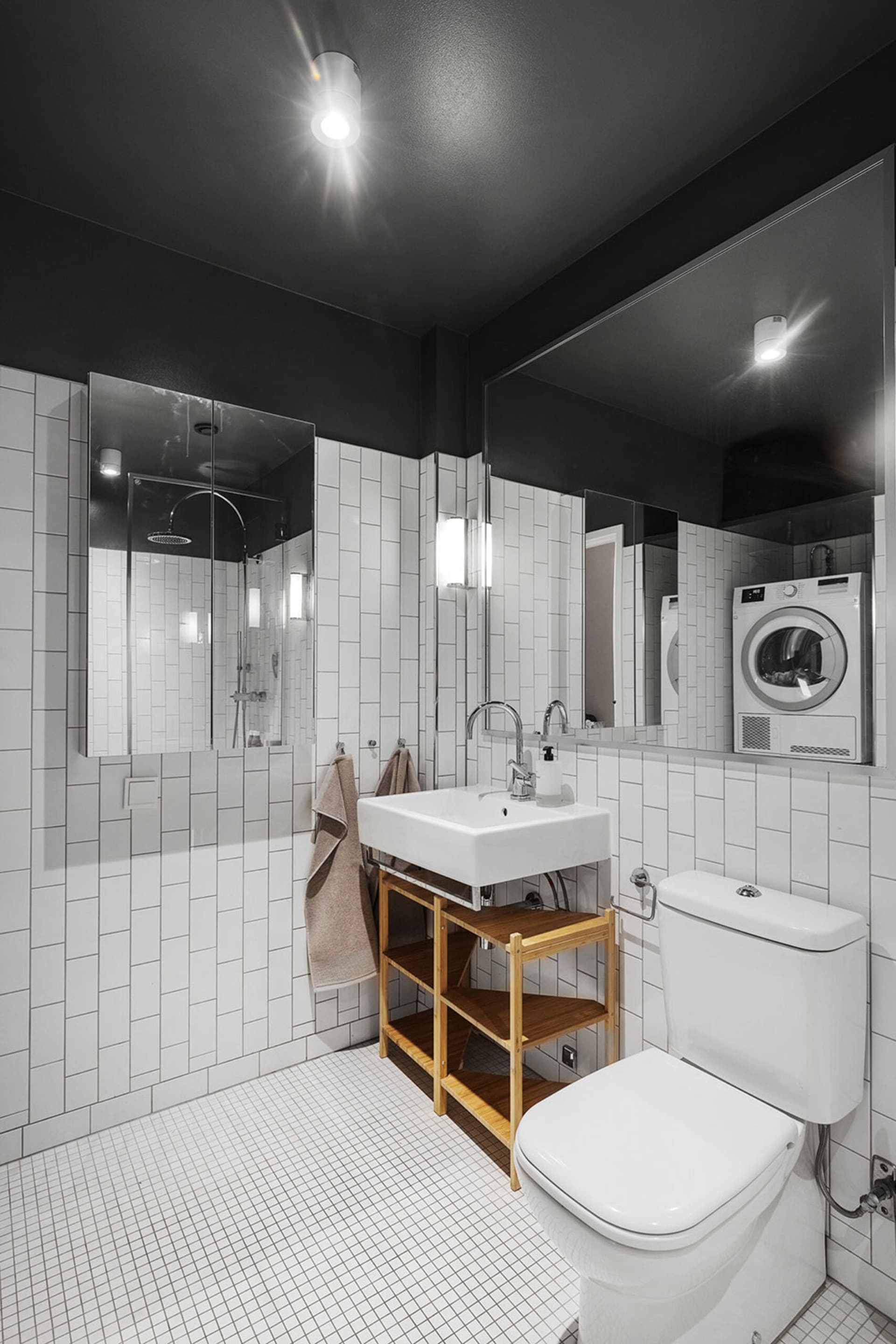 A minimalist bathroom with white tiles, a wooden shelf, and a glass shower enclosure.