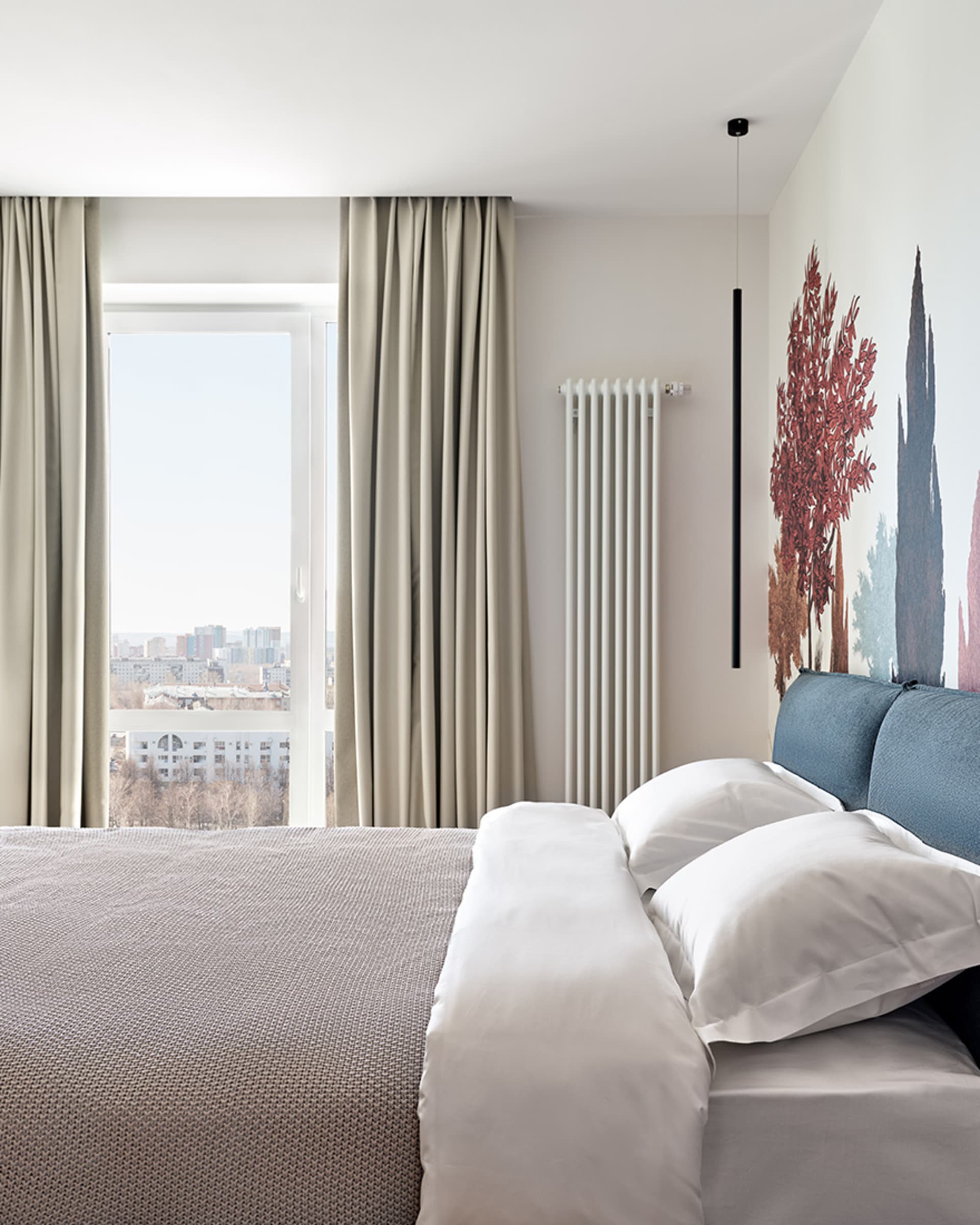A minimalist white bedroom with a blue bed headboard, white bedding, and curtains