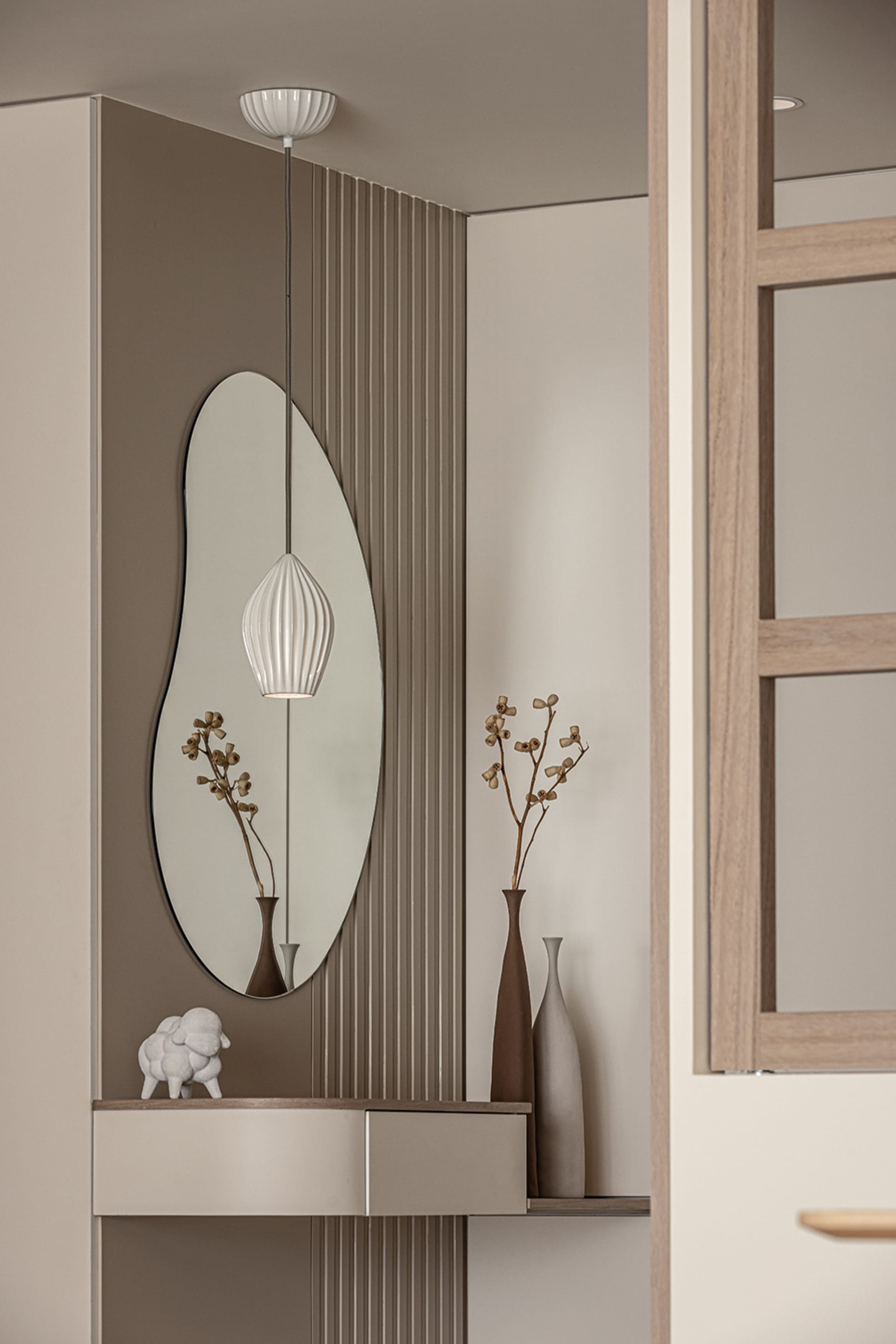 A modern entryway featuring a frameless oval mirror, a white pendant light, and decorative vases.