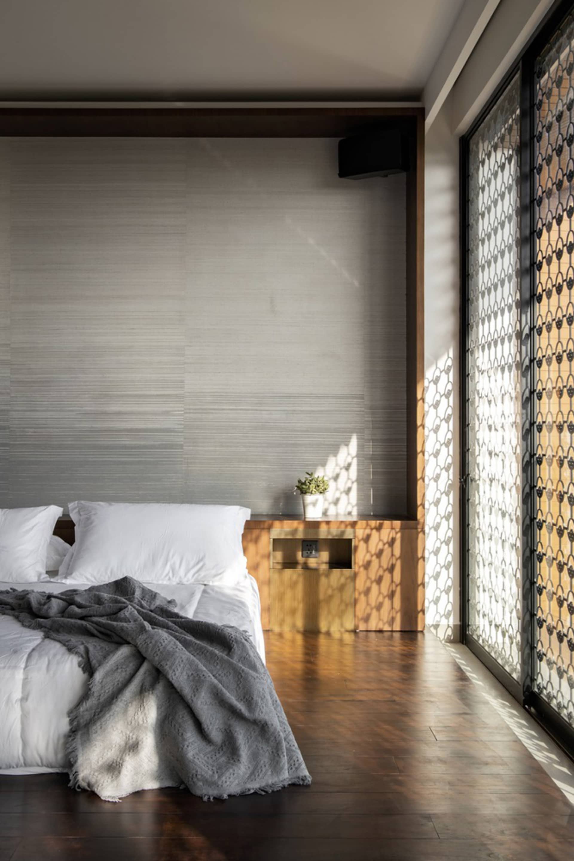 A minimalist bedroom with a wooden floor, white bedding, and a wooden nightstand with a small plant.