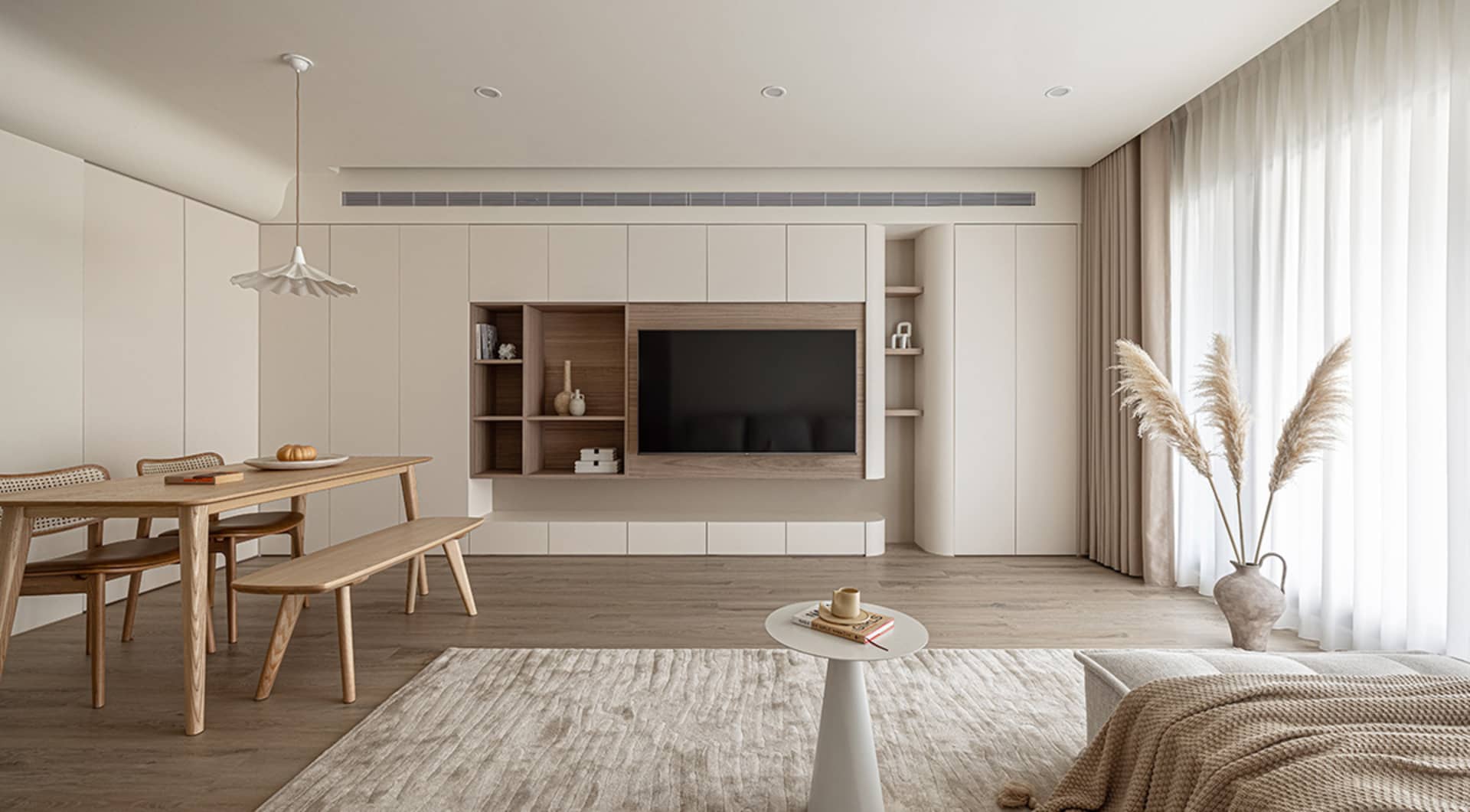 A minimalist living room featuring a wall-mounted television, wooden furniture, and beige accents.