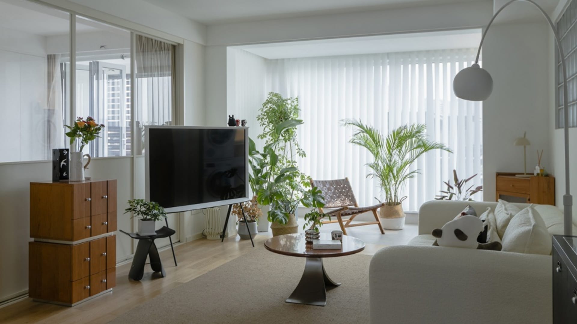A minimalist living room with neutral tones, featuring a white sofa, black coffee table, and potted plants.