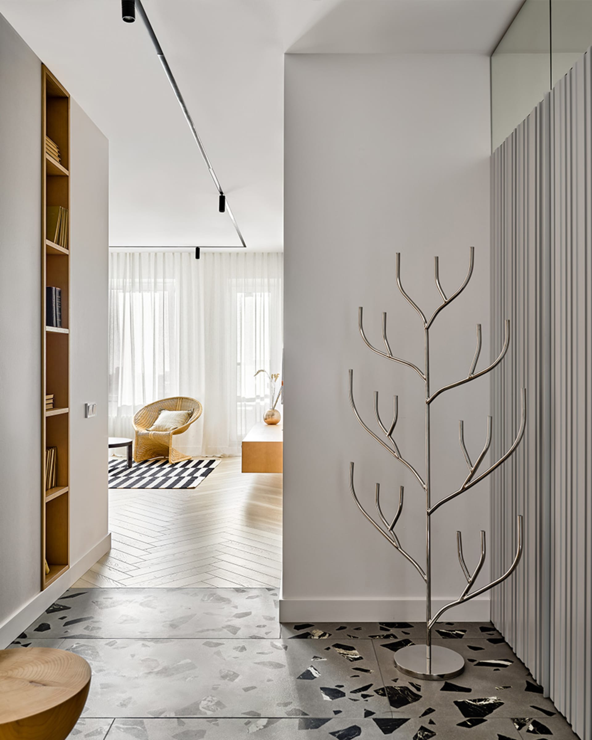Modern interior design featuring contemporary furniture, a stylish coat rack made of metallic branches, and a white terrazzo