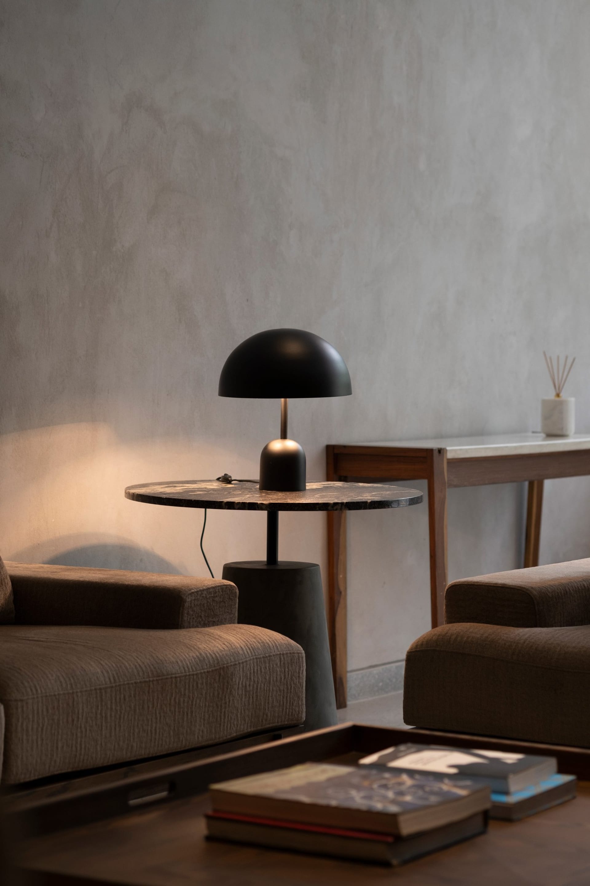 A modern living room featuring a round marble table with a black lamp, two plush brown sofas, and coffee table with books.