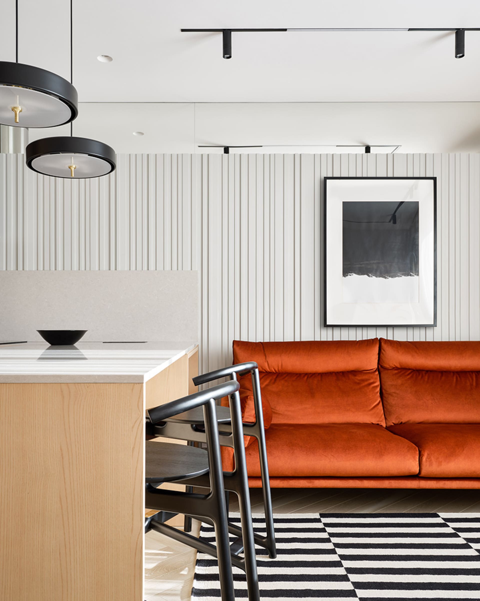 A modern living room with textured wallpaper, an orange sofa, and a black and white striped rug.
