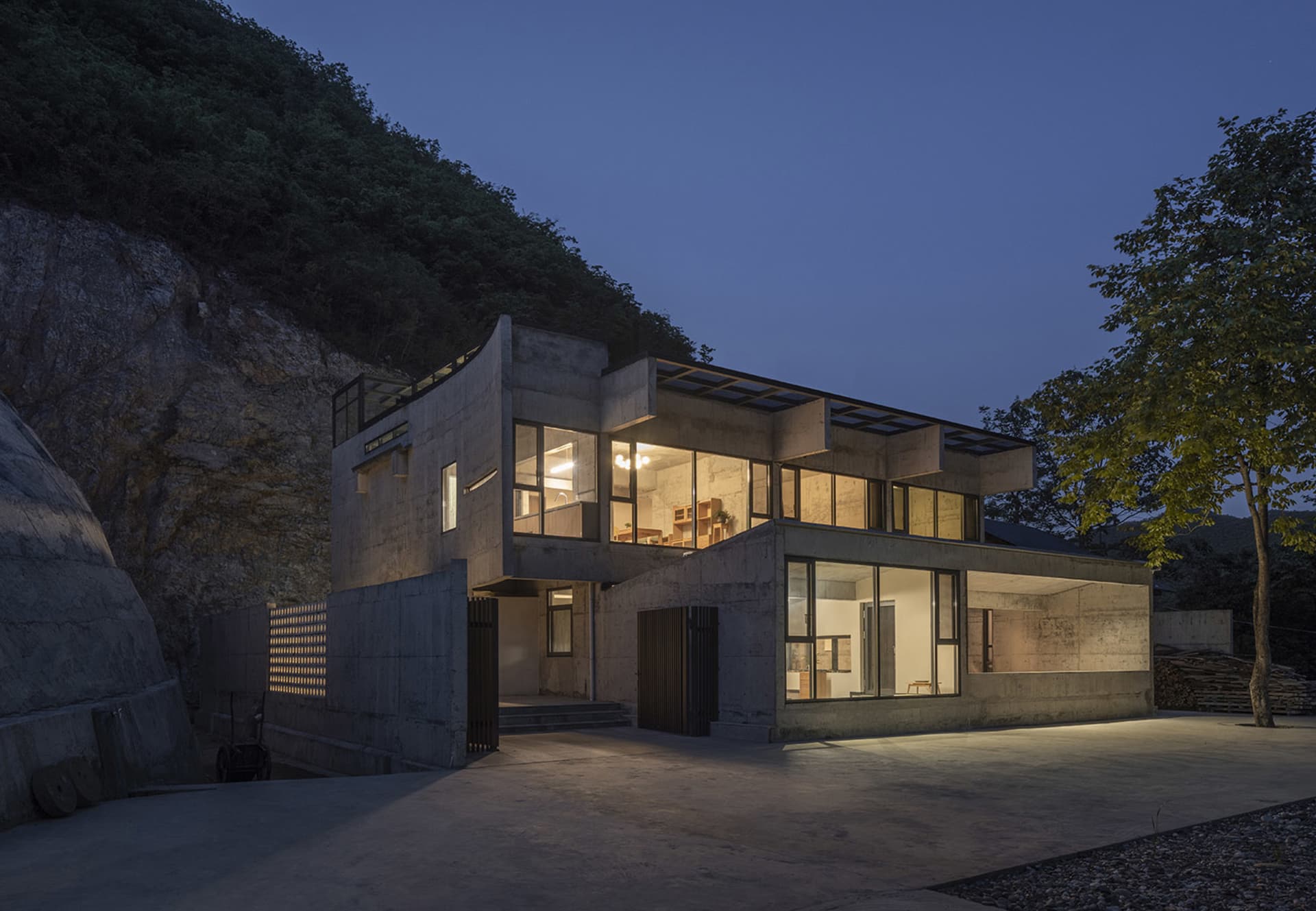 A modern house built into a hillside with concrete walls and large glass windows.