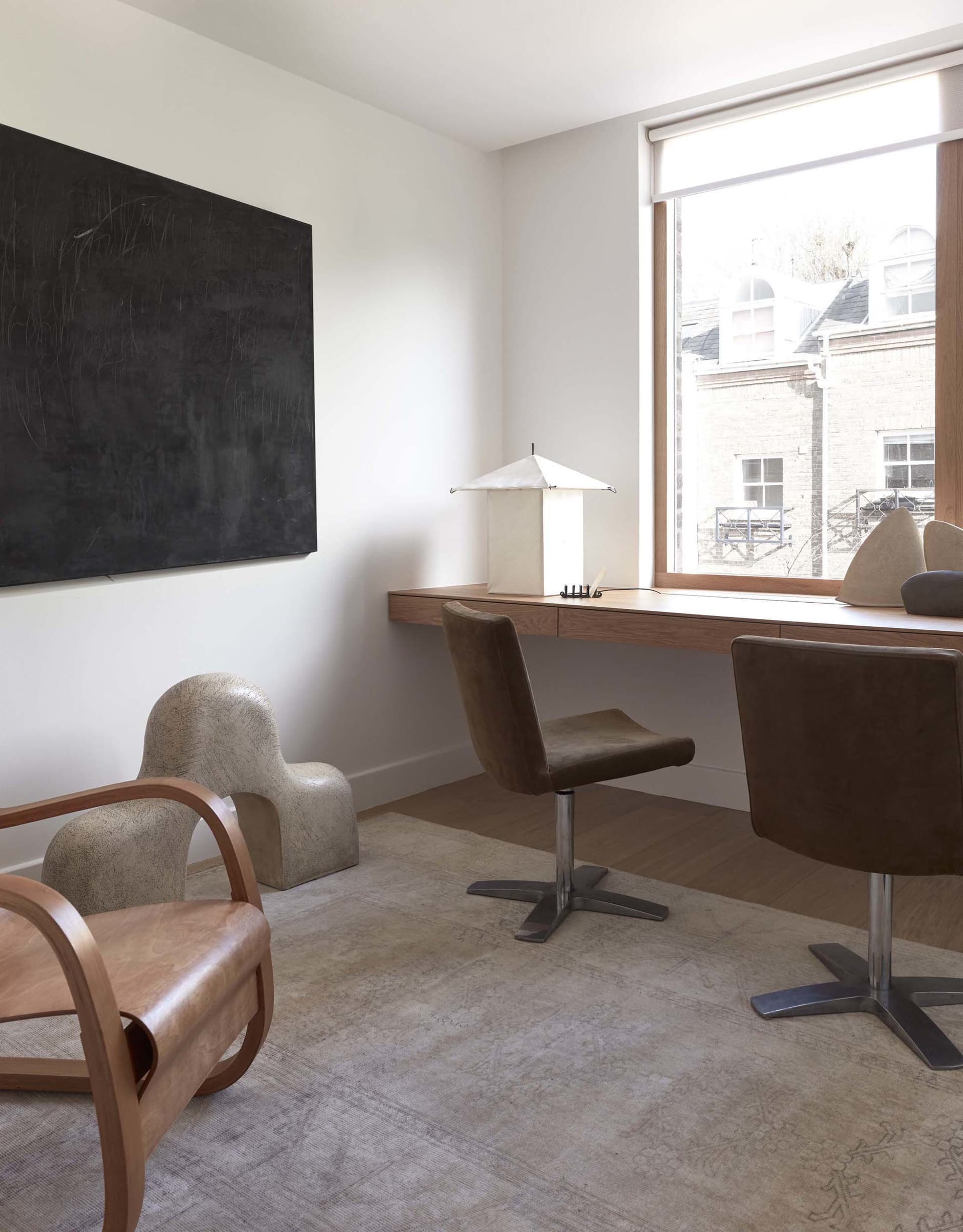 A modern home office featuring a sleek desk, stylish chairs, and a large window with a view of the outside.