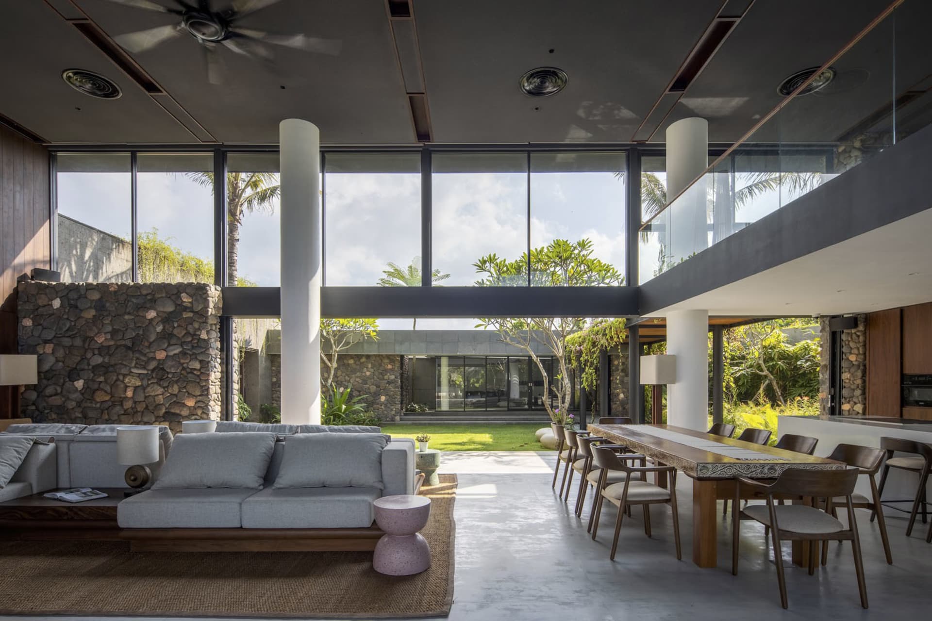 A modern living and dining space with garden views, featuring a combination of glass, wood, and stone materials.