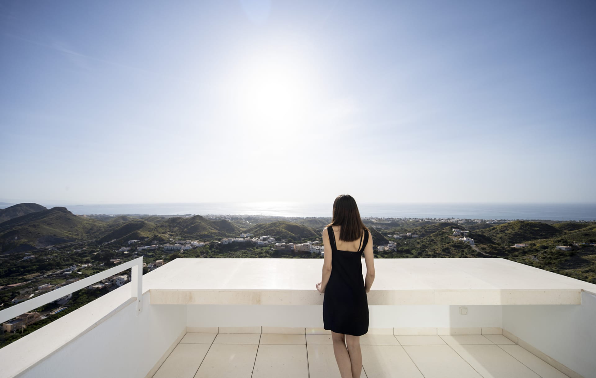 A woman standing on a modern terrace overlooking a scenic view of hills and the sea.