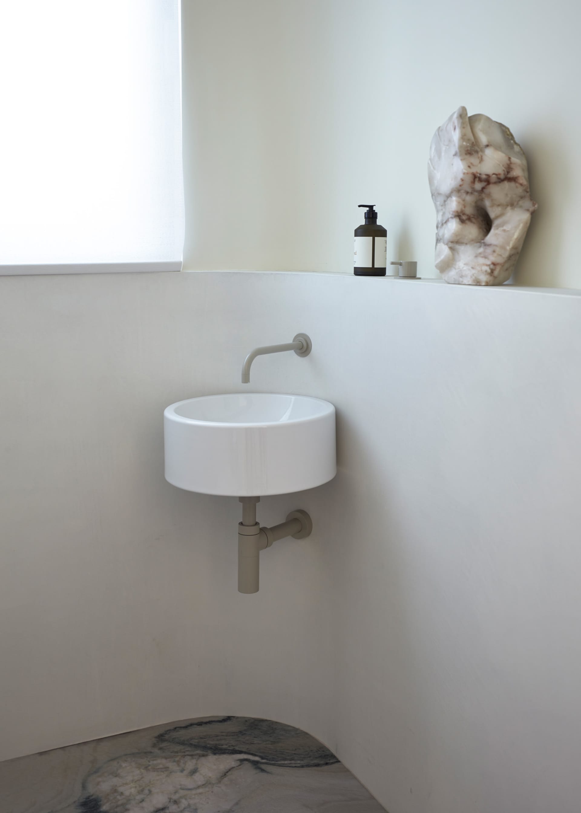 A minimalist modern bathroom with a circular sink, marble sculpture, and bottle of liquid.