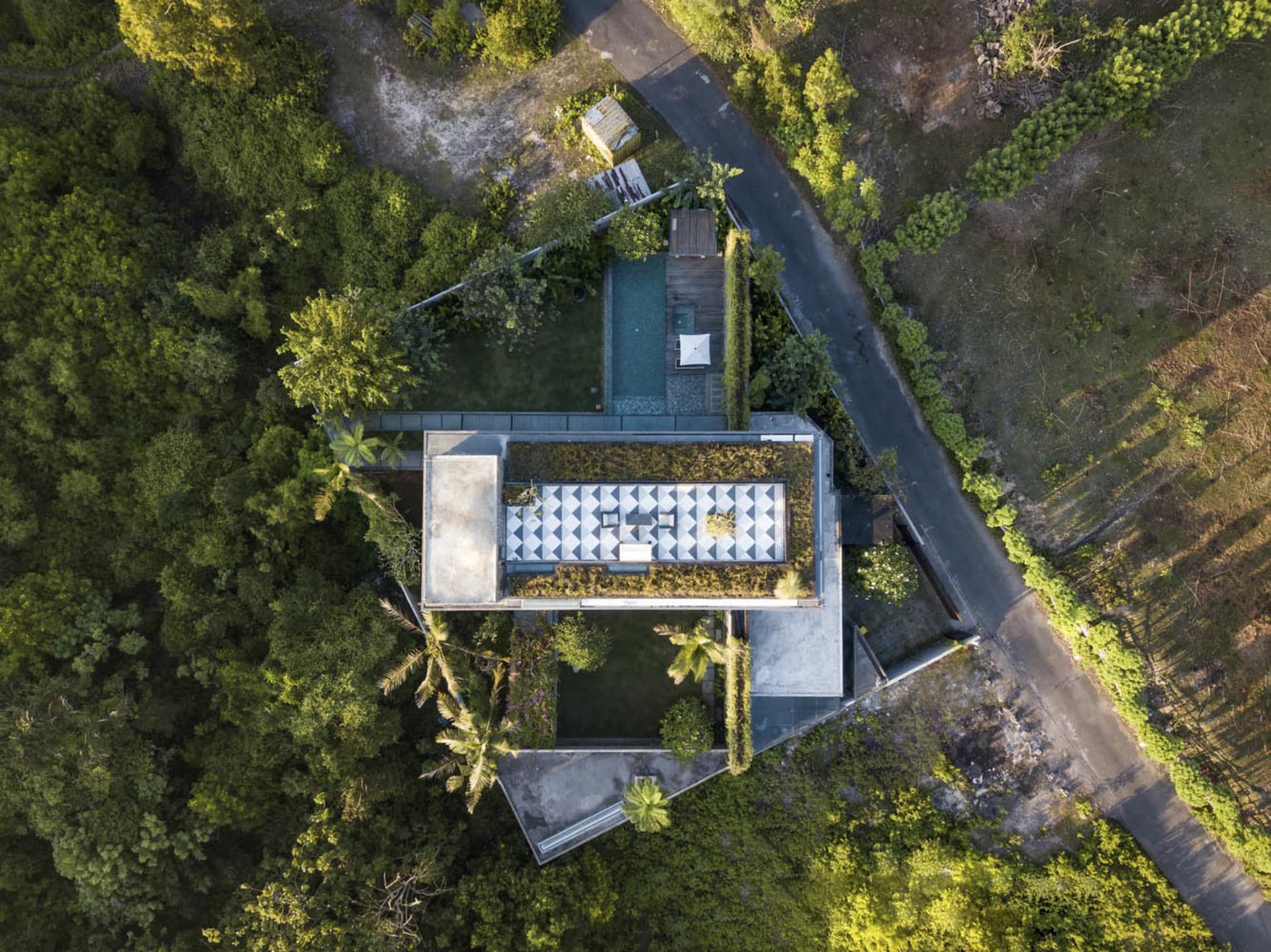 Aerial view of a modern house with a concrete exterior and lush greenery.