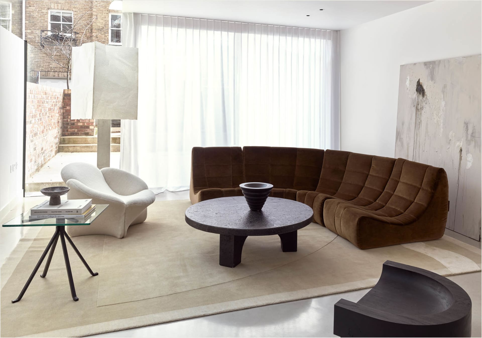 Modern living room featuring a sleek, brown velvet sofa and a round stone coffee table in a minimalist interior design settin