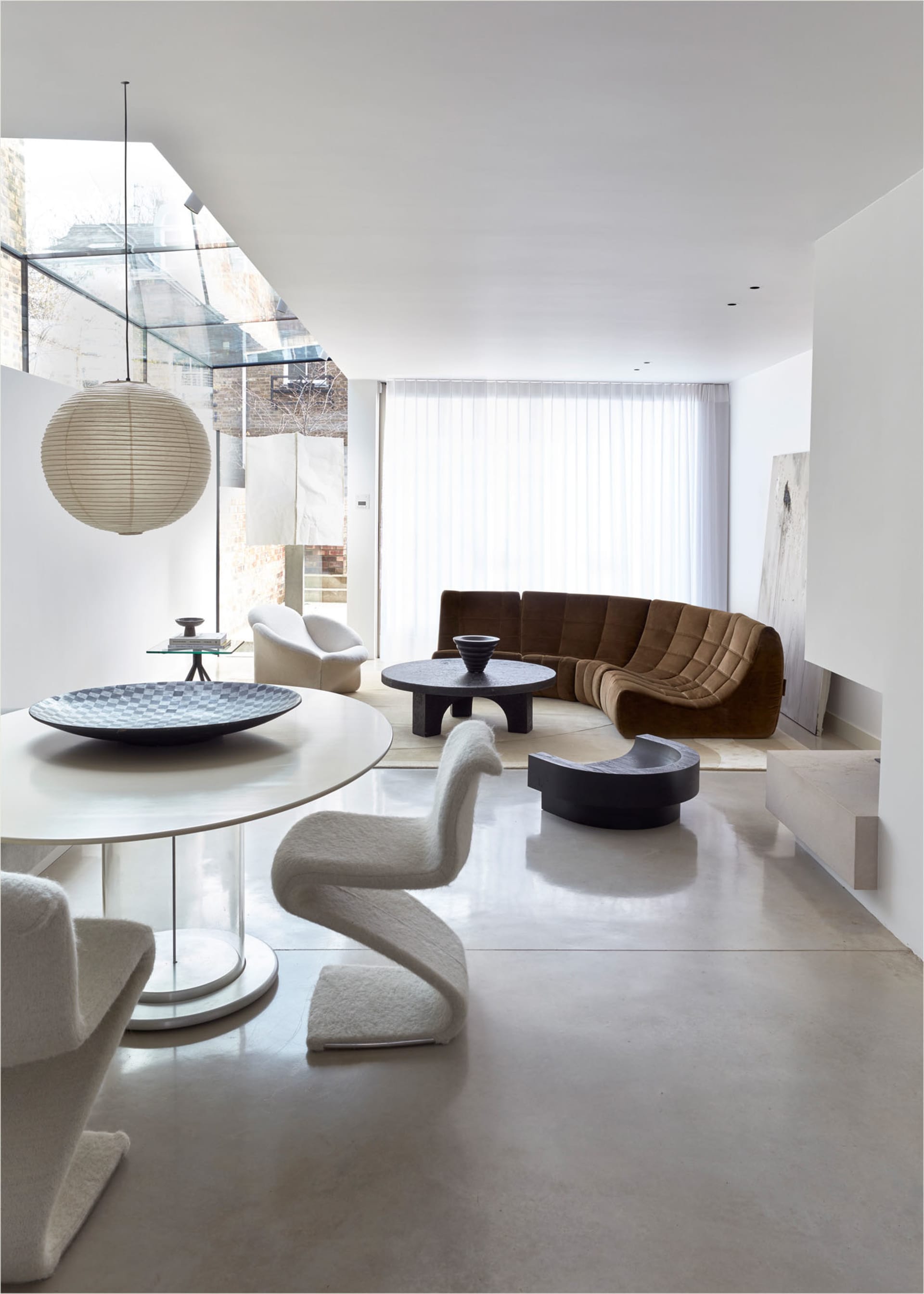 A minimalist living room with white walls, a curved sofa, a round table, and white chairs.